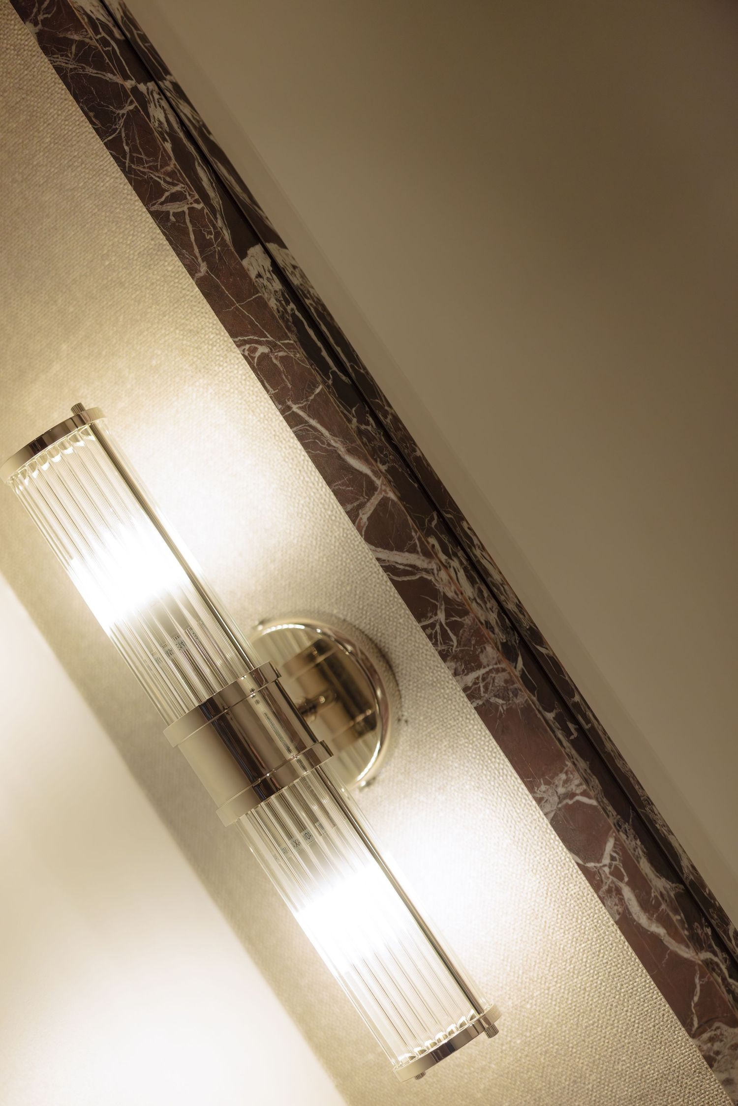 Modern wall sconce with frosted glass tube shade mounted on marble wall creates elegant ambient lighting.