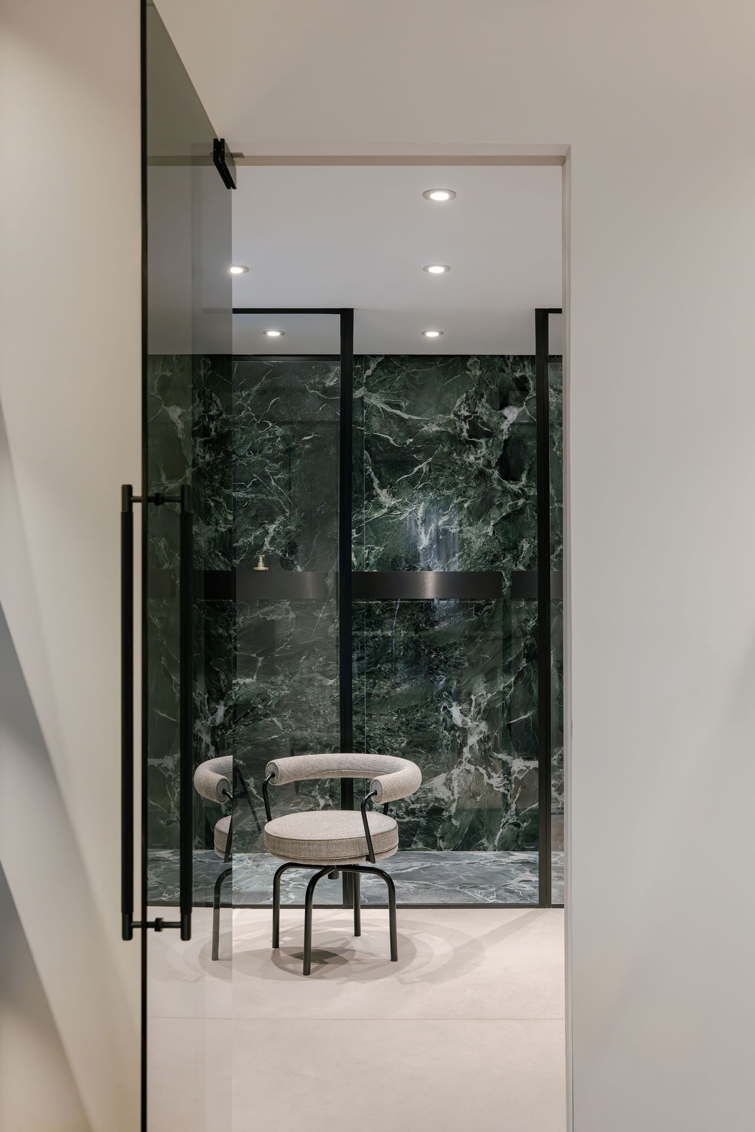 Modern white hallway with dark marble walls and recessed lighting leads to a minimalist seating area by INKA Studio.