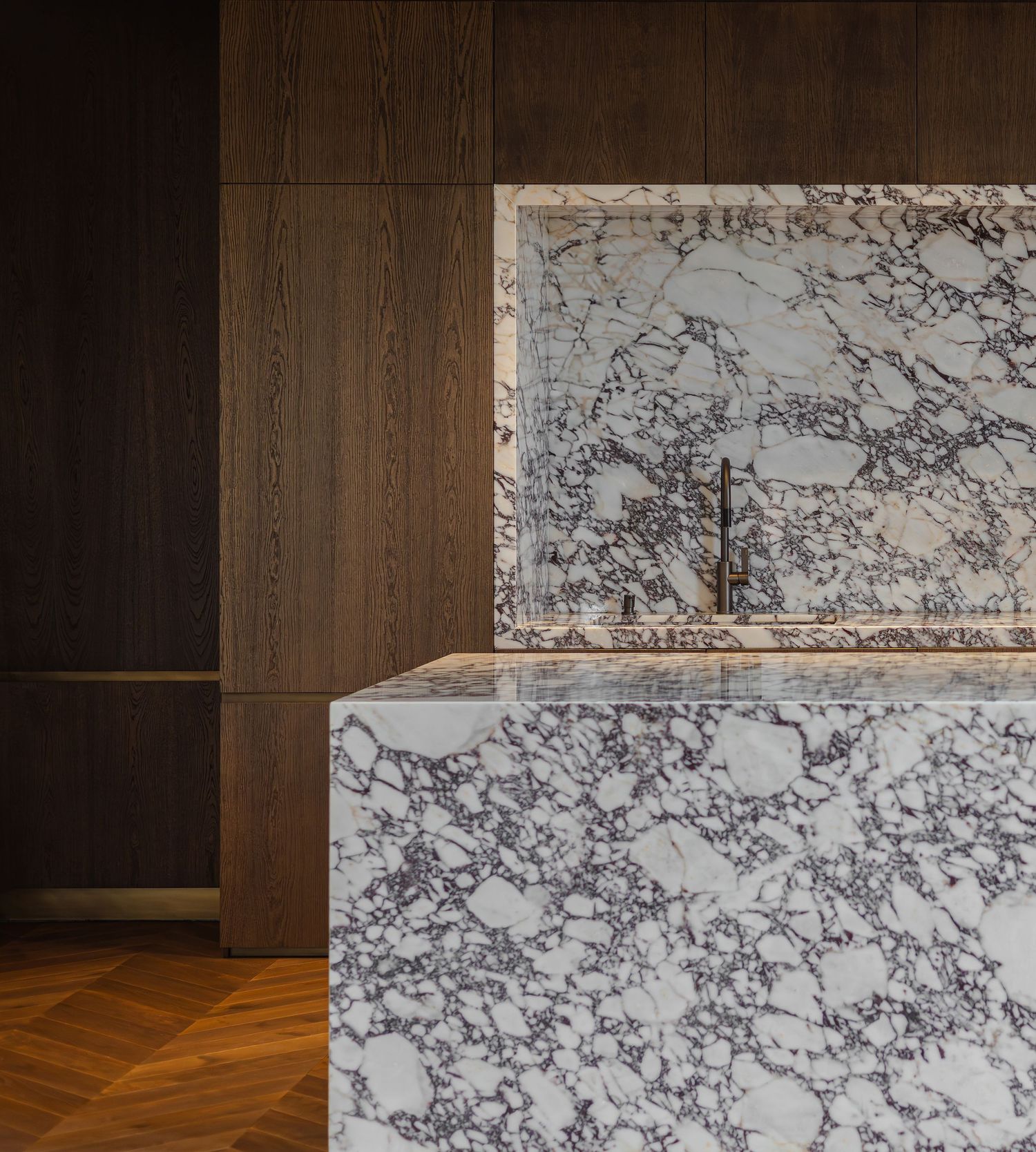 Architectural detail showing a wooden wall panel meeting white marble with gray veining in a modern interior space by Slavica Citakovic.