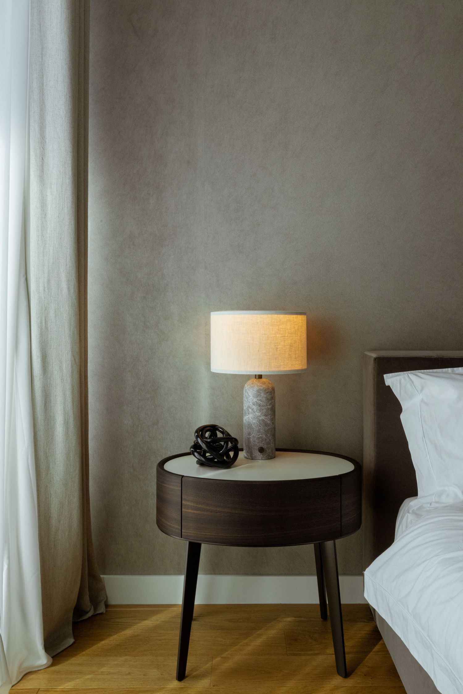 Modern hotel bedroom interior with round side tables, white bedding, and table lamps against gray textured walls by Studio Fluid.