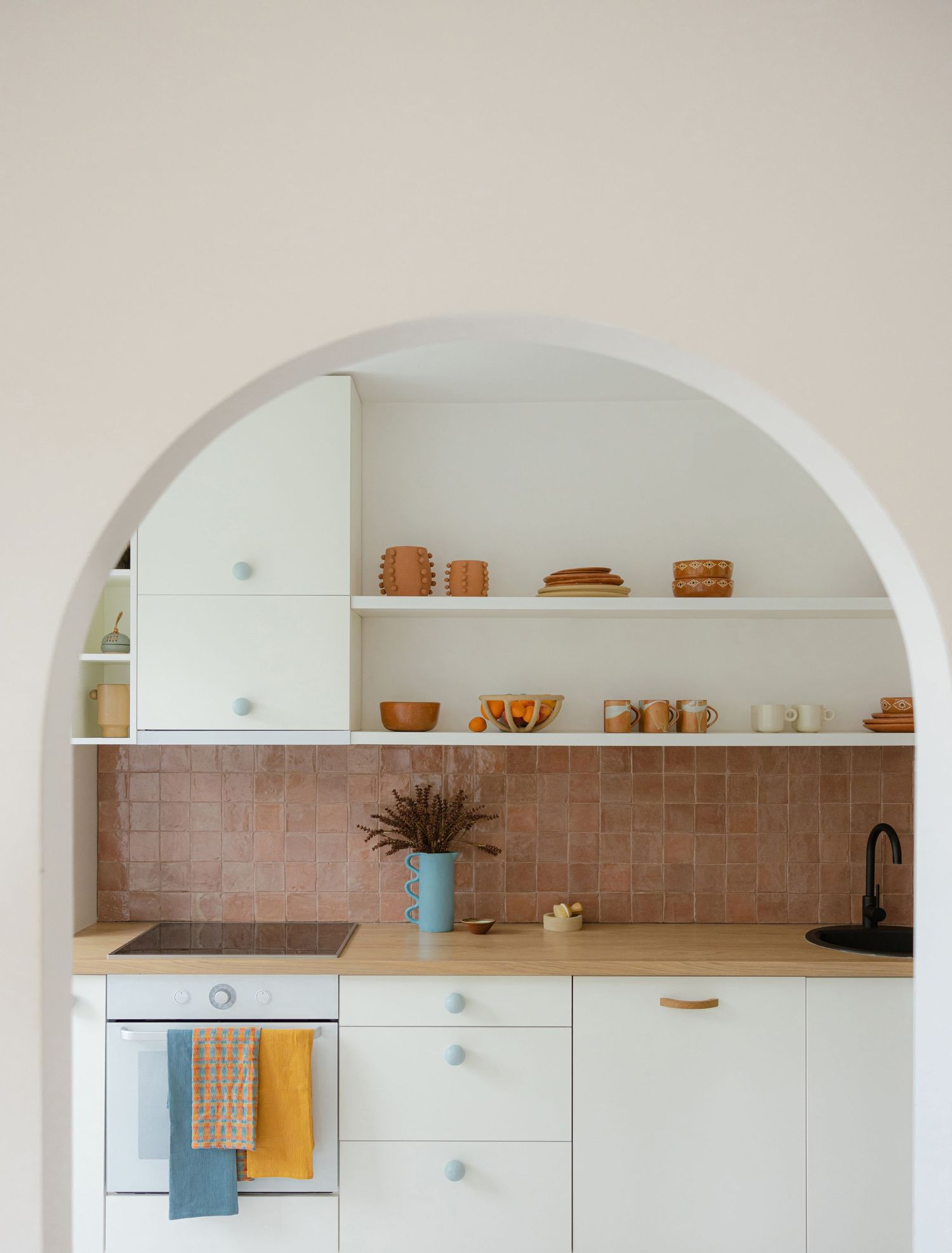 Modern white kitchen with arched alcove shelving displaying terracotta pottery and minimalist cabinetry by Maja Interiors.