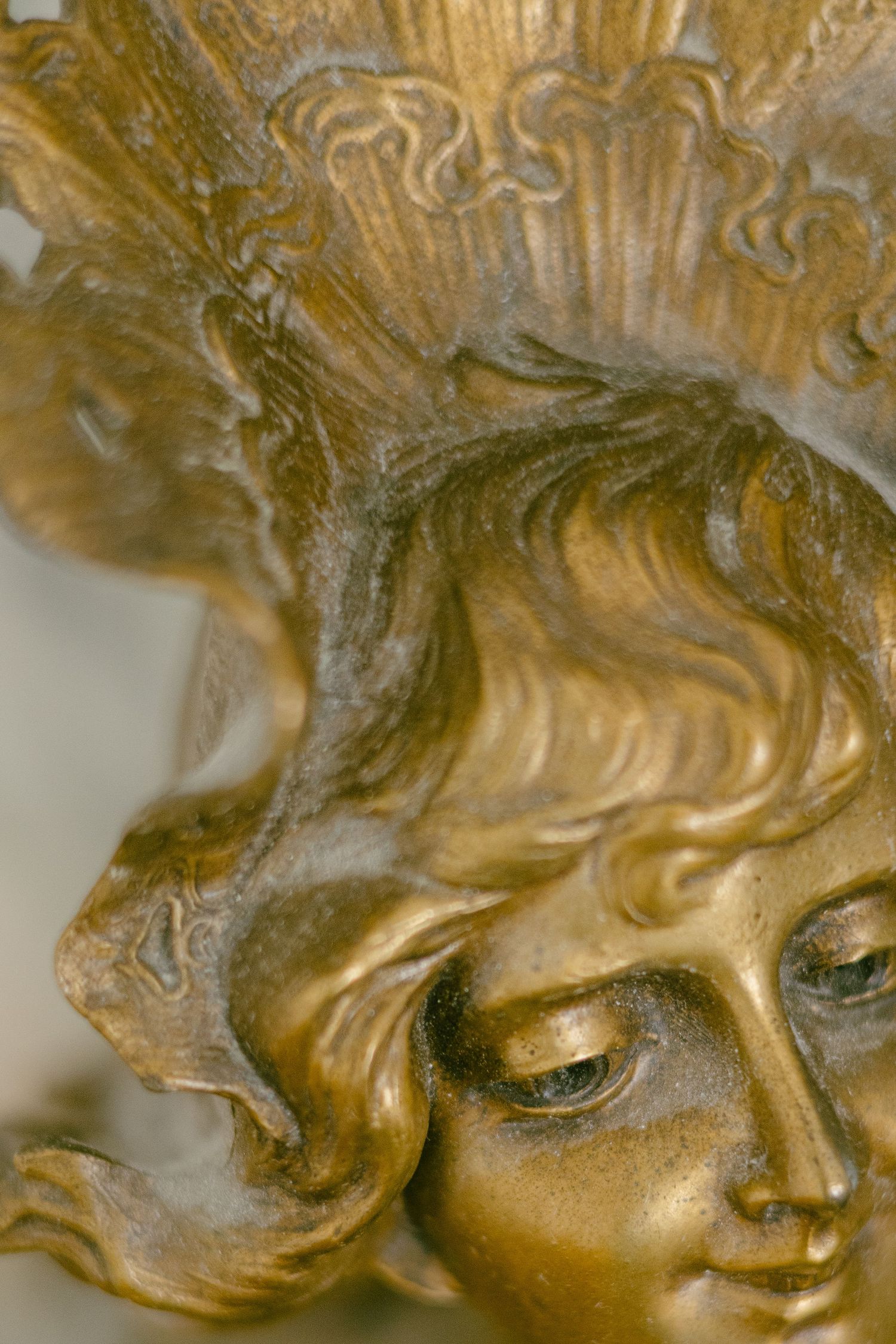 Close-up of a golden Art Nouveau bronze sculpture featuring a woman's face with flowing hair and ornate headdress.