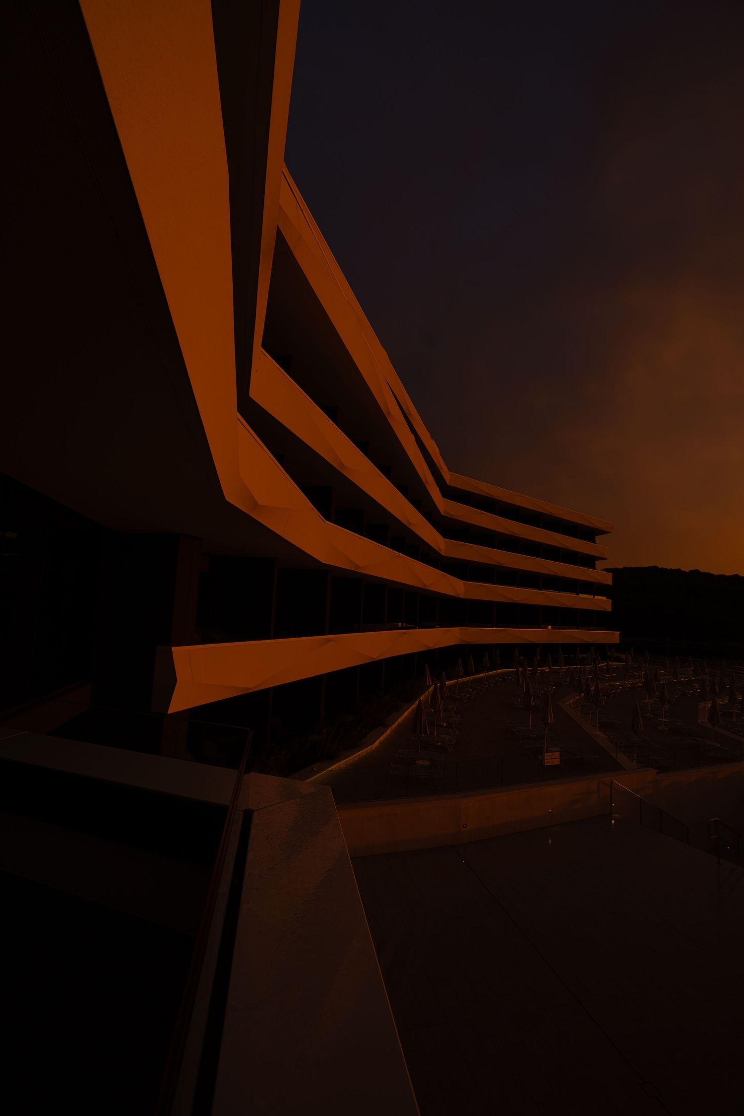 Modern building architecture illuminated by warm orange lights at dusk, with dramatic angular lines against a dark sky.