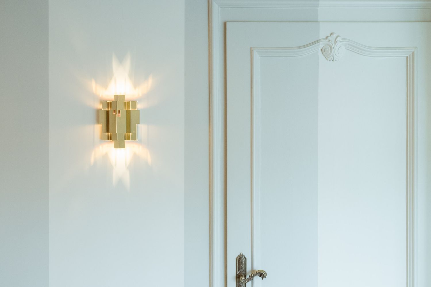 A modern white interior with gold sconces and elegant molding details on the walls.