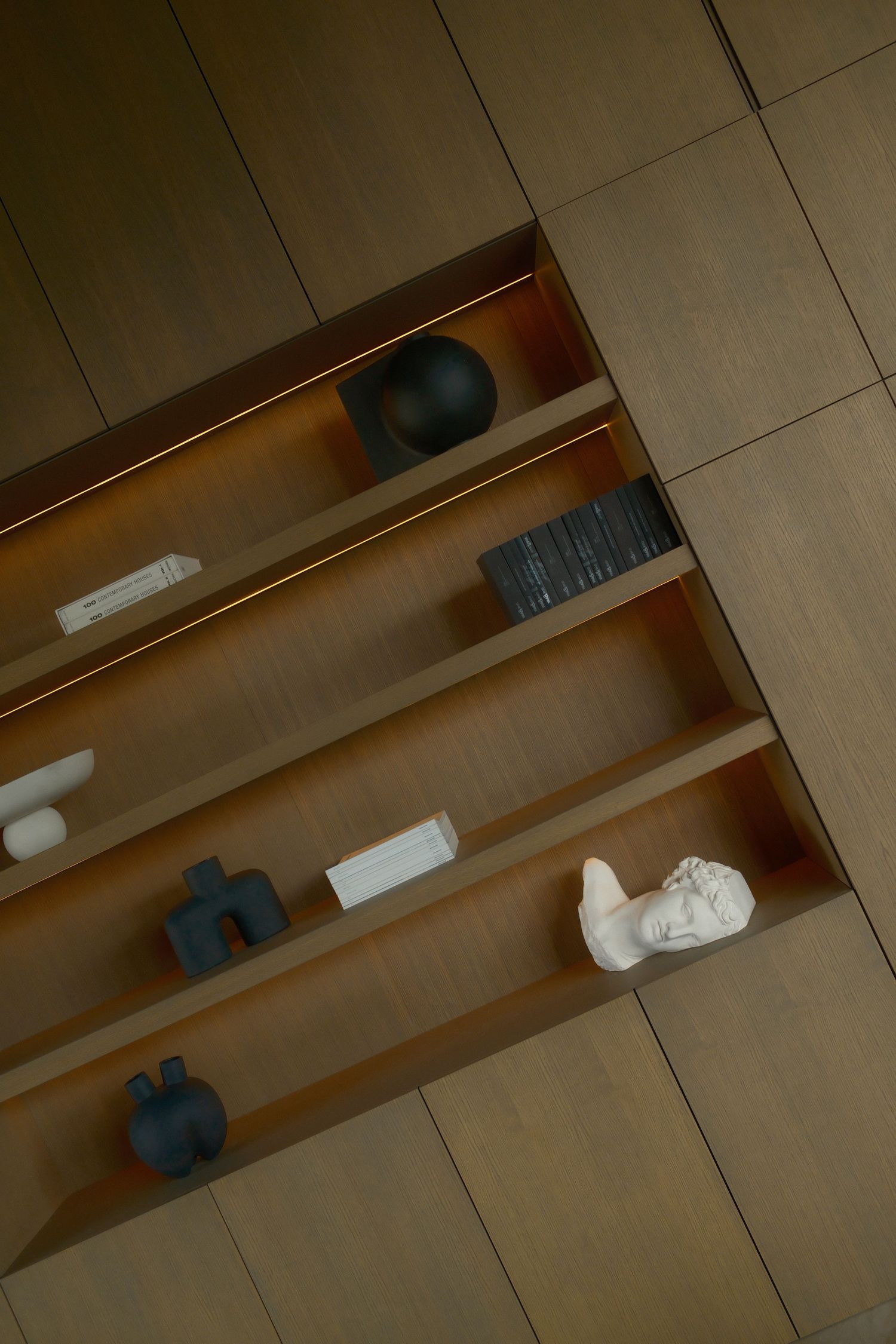 Modern wooden built-in shelves with accent lighting displaying decorative sculptures and art objects.