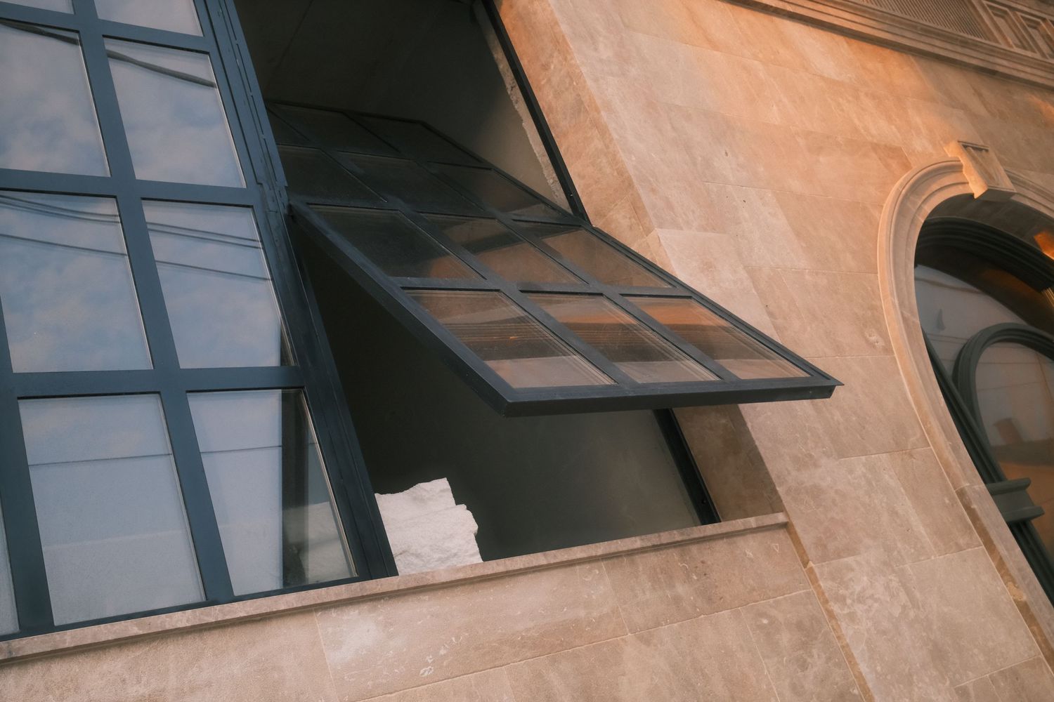 A row of old-style industrial windows with tilted panes mounted on a textured beige wall in natural lighting.