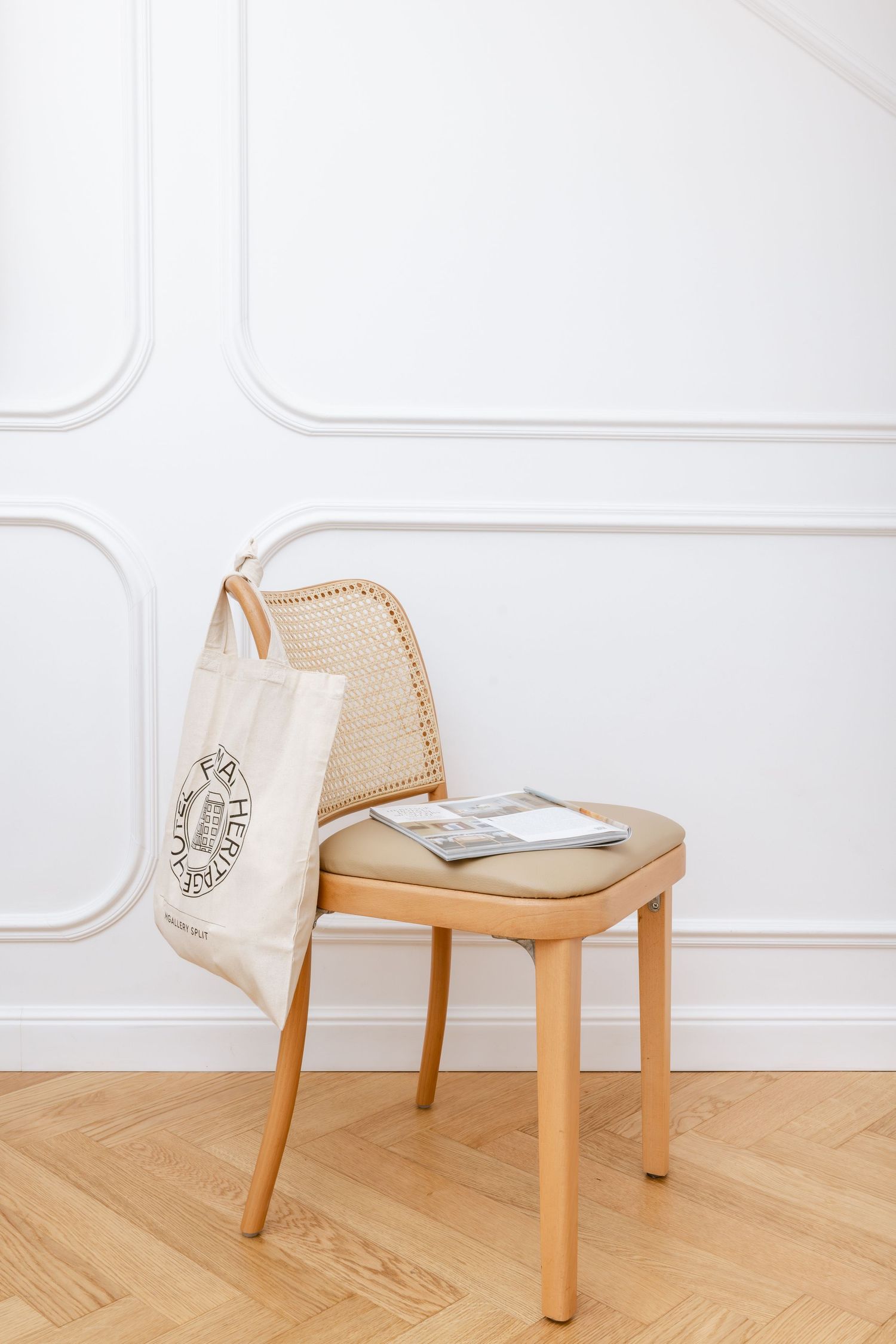 Wooden chair with woven backrest and white cushion seat shown in sequence against white paneled wall featuring Vogue Adria. Hotel Fermai
