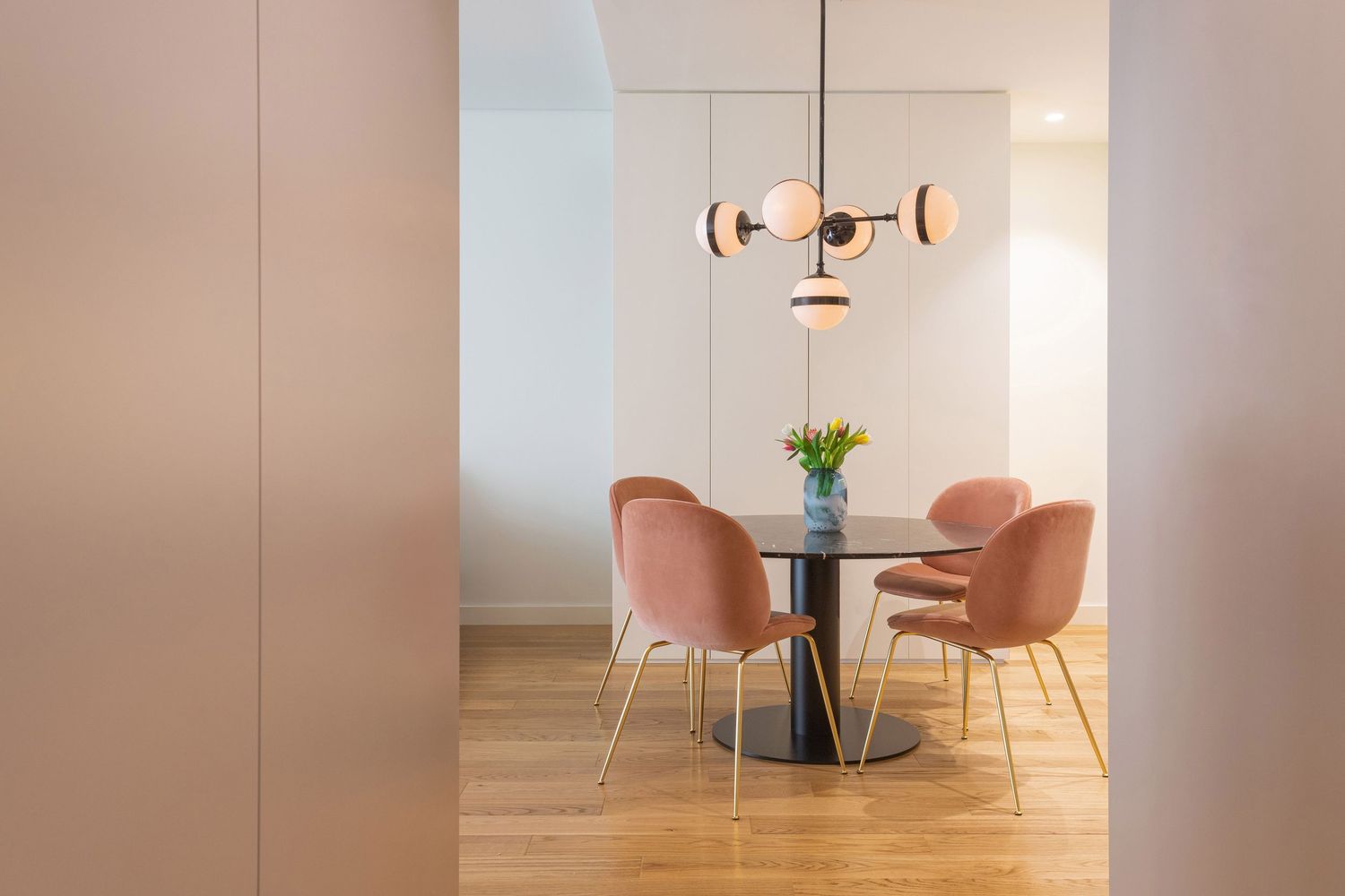 Minimalist dining room interior with pink chairs and round table against beige walls and warm lighting by Studio Fluid.