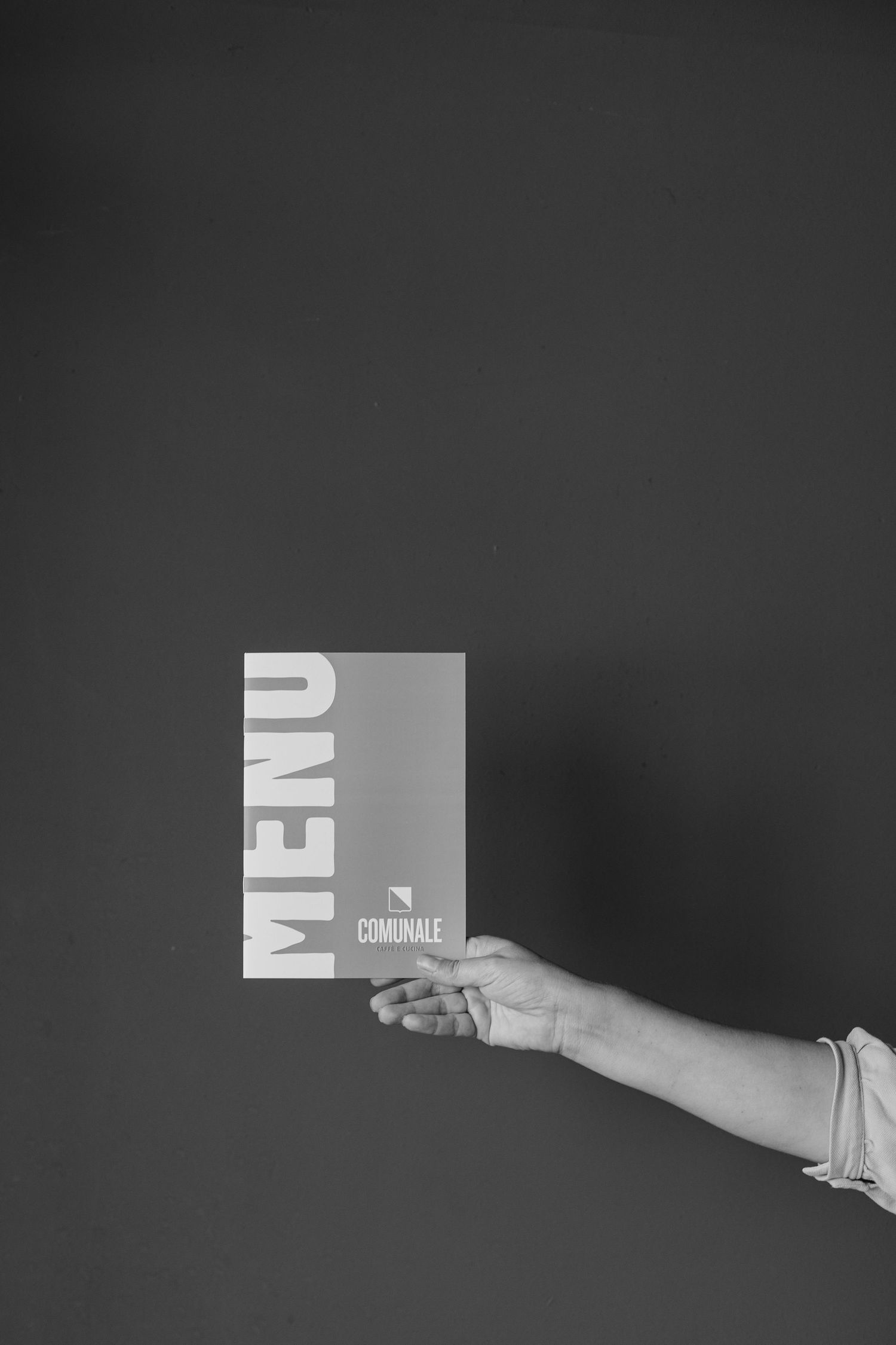 A hand holds a white card or paper against a dark background in a minimalist black and white composition.