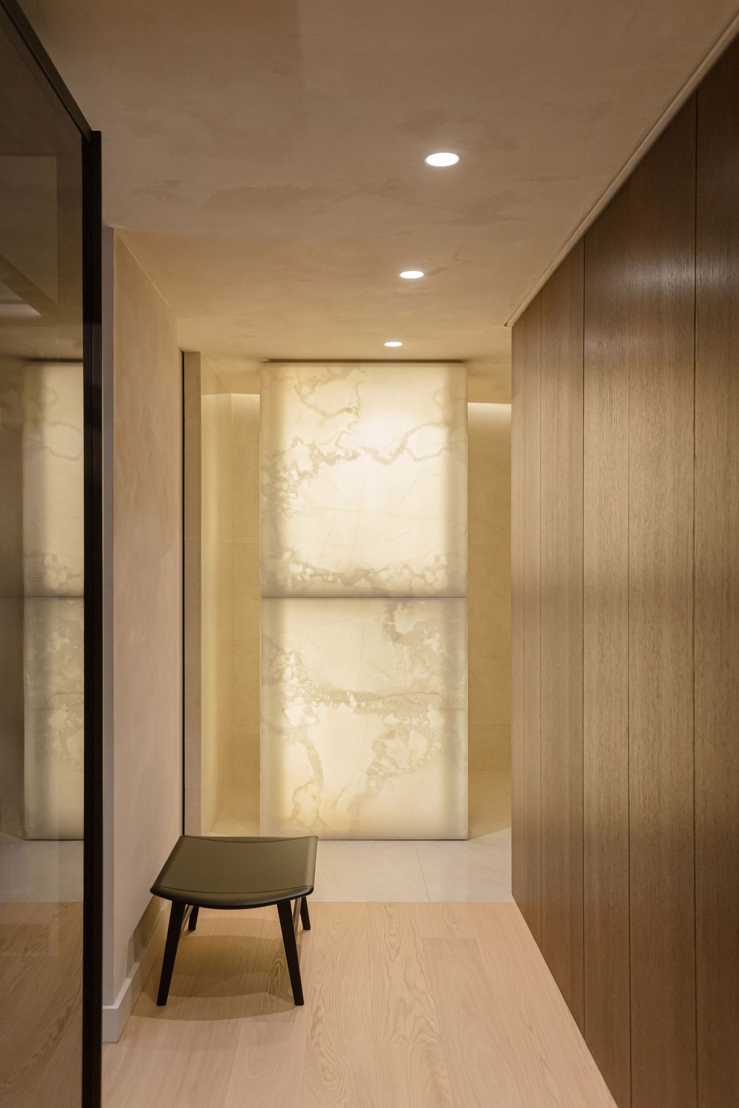 Modern hallway interior with wooden paneling, recessed lighting, and abstract wall art illuminated by ambient lighting by Studio Fluid.