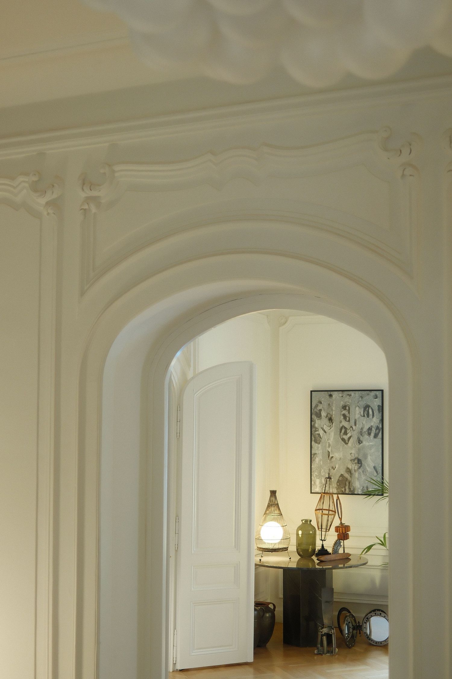 Elegant white archway leading to a room with decorative artwork and a glowing lamp on a side table.