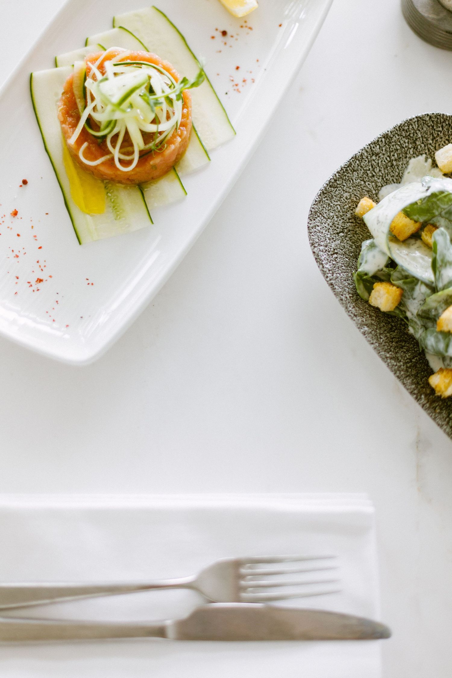 Close-up of elegant plated appetizers on white rectangular dishes with delicate garnishes and sauces.