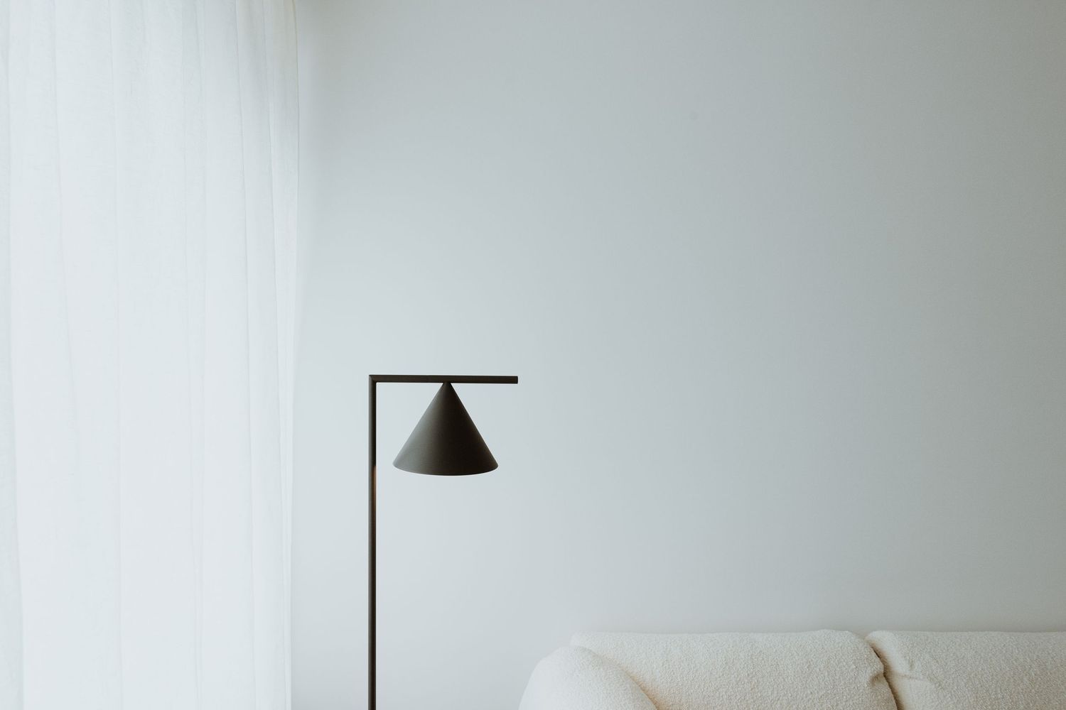 Minimalist living room corner with Flos Captain Flint black floor lamp designed by Michael Anastassiades and white sofa against white wall.