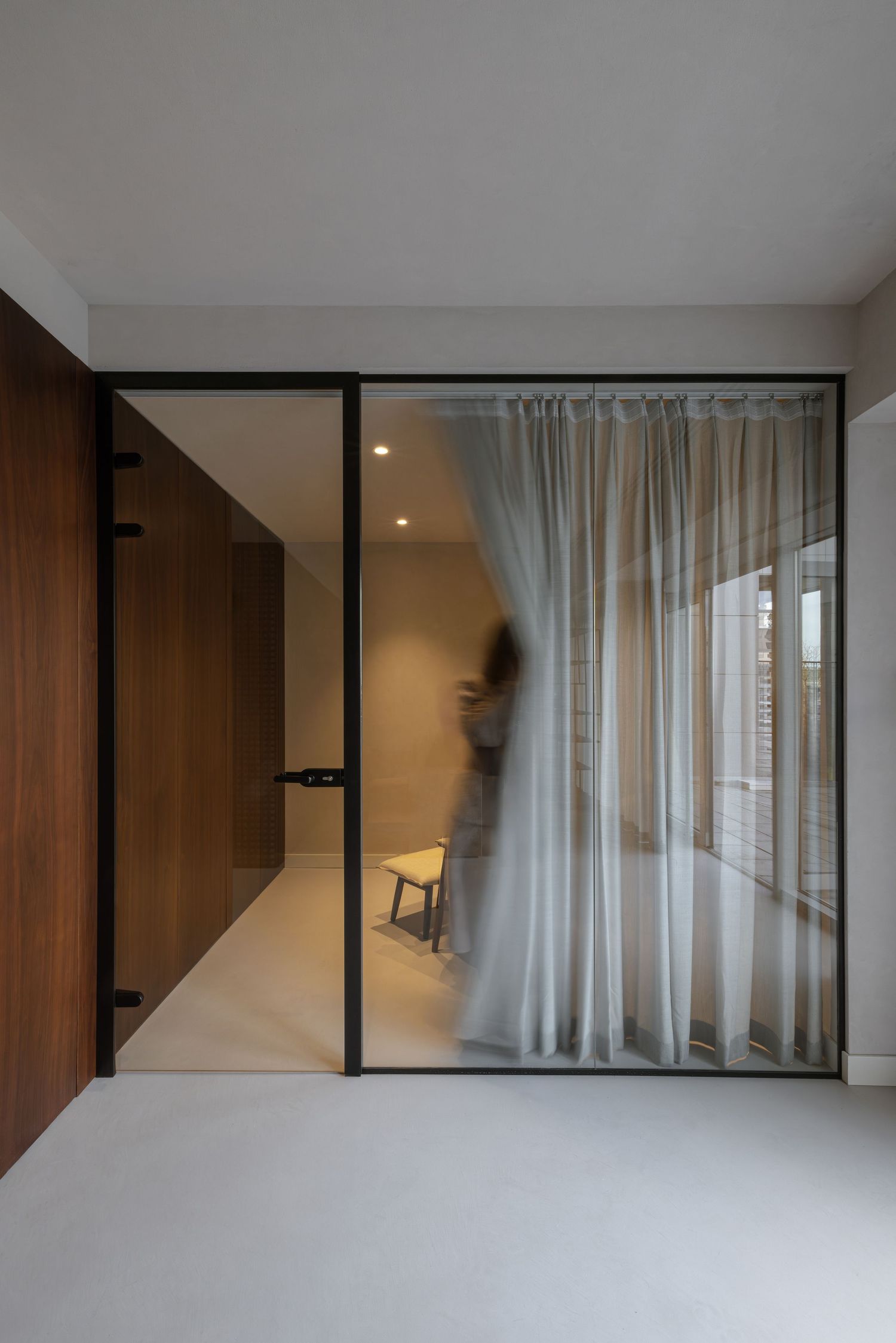 Modern minimalist interior with white walls, glass partitions, and sheer curtains creating a sleek, open living space by Studio Fluid.
