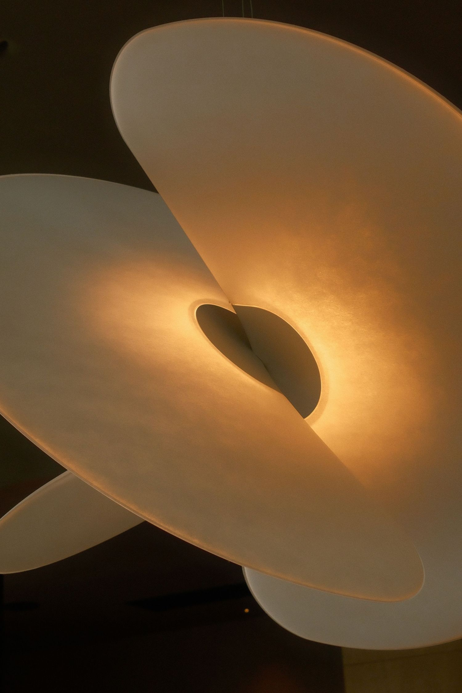 Modern sculptural pendant light fixture with overlapping curved white panels glowing warm amber light.