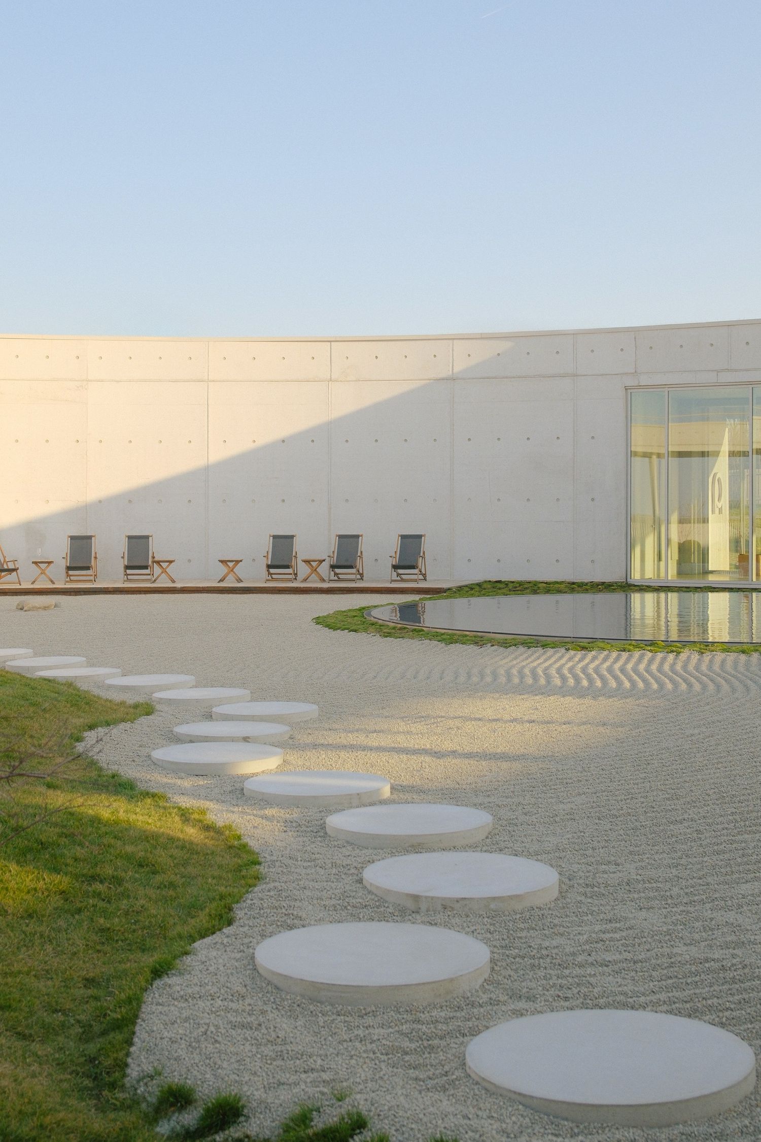 Modern building exterior with a series of circular concrete platforms arranged in a curved pattern along a gravel path.