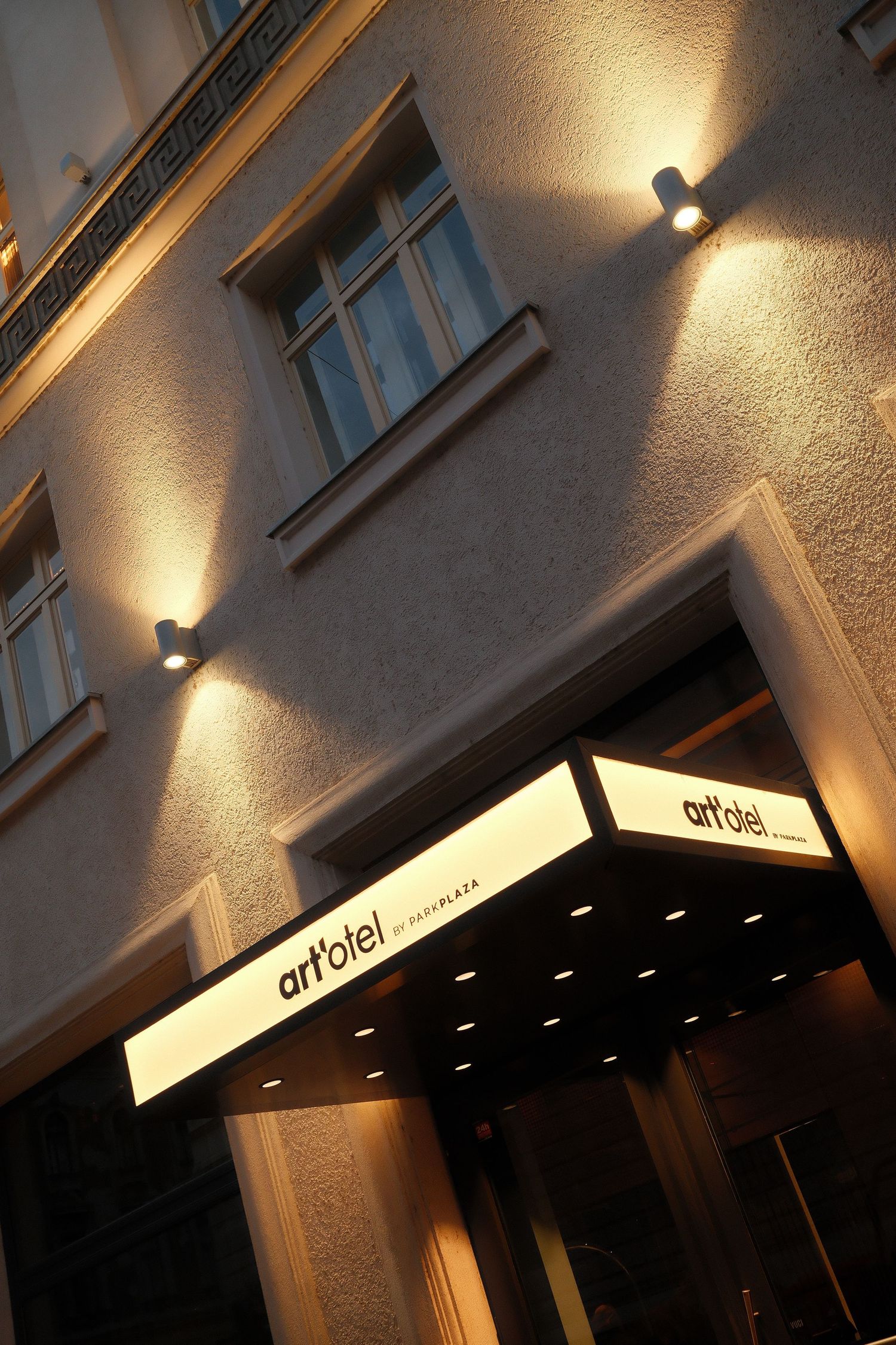 Illuminated exterior of Art Hotel entrance with spotlights casting warm glow on textured wall and modern signage at night.
