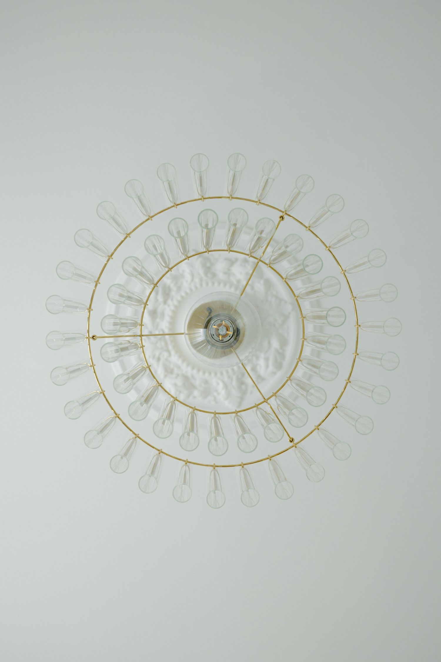 Gold circular chandelier with multiple clear bulbs arranged in concentric rings mounted on white ceiling.