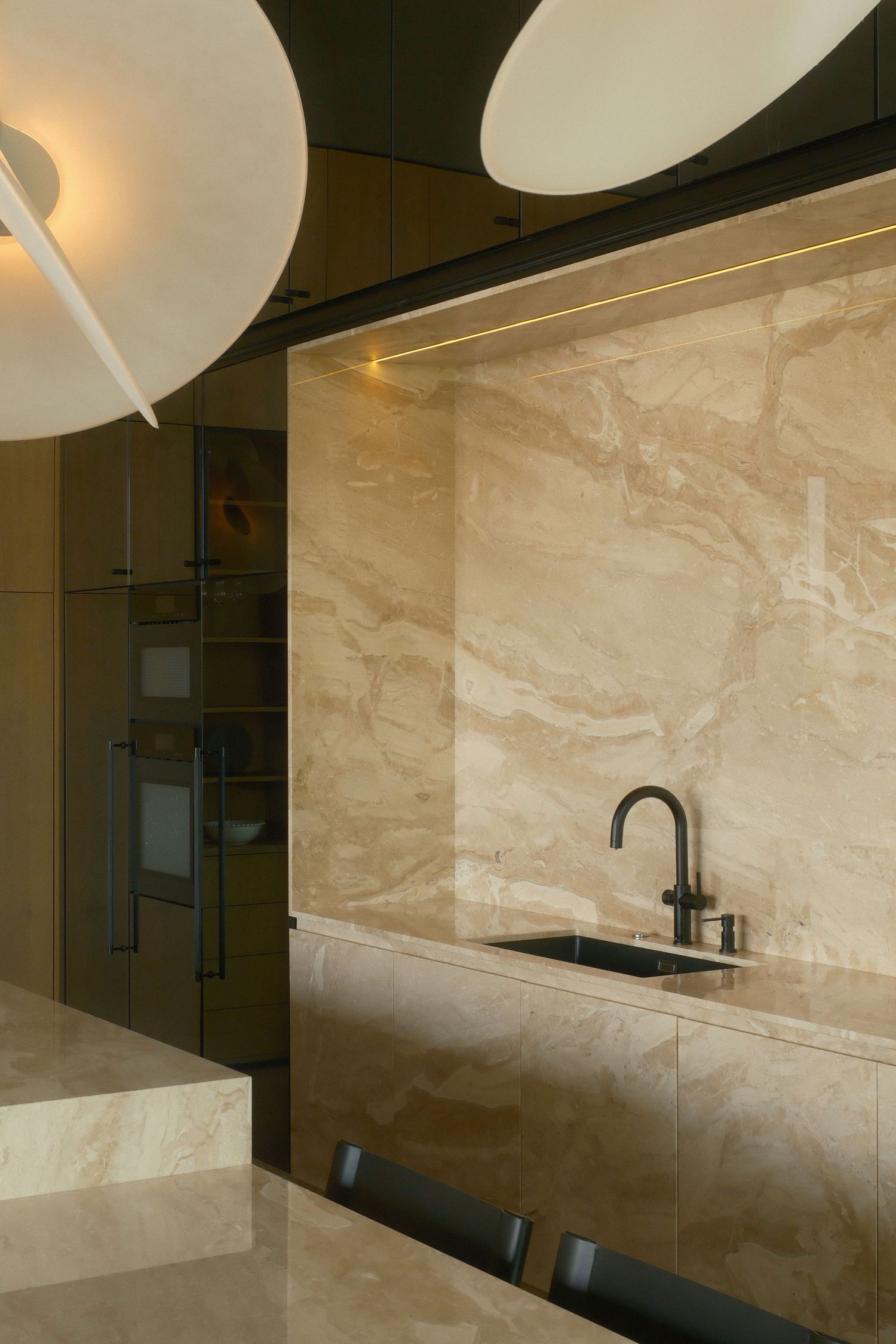 Modern kitchen with beige marble backsplash, black faucet, undermount sink, and elegant circular ceiling lights.