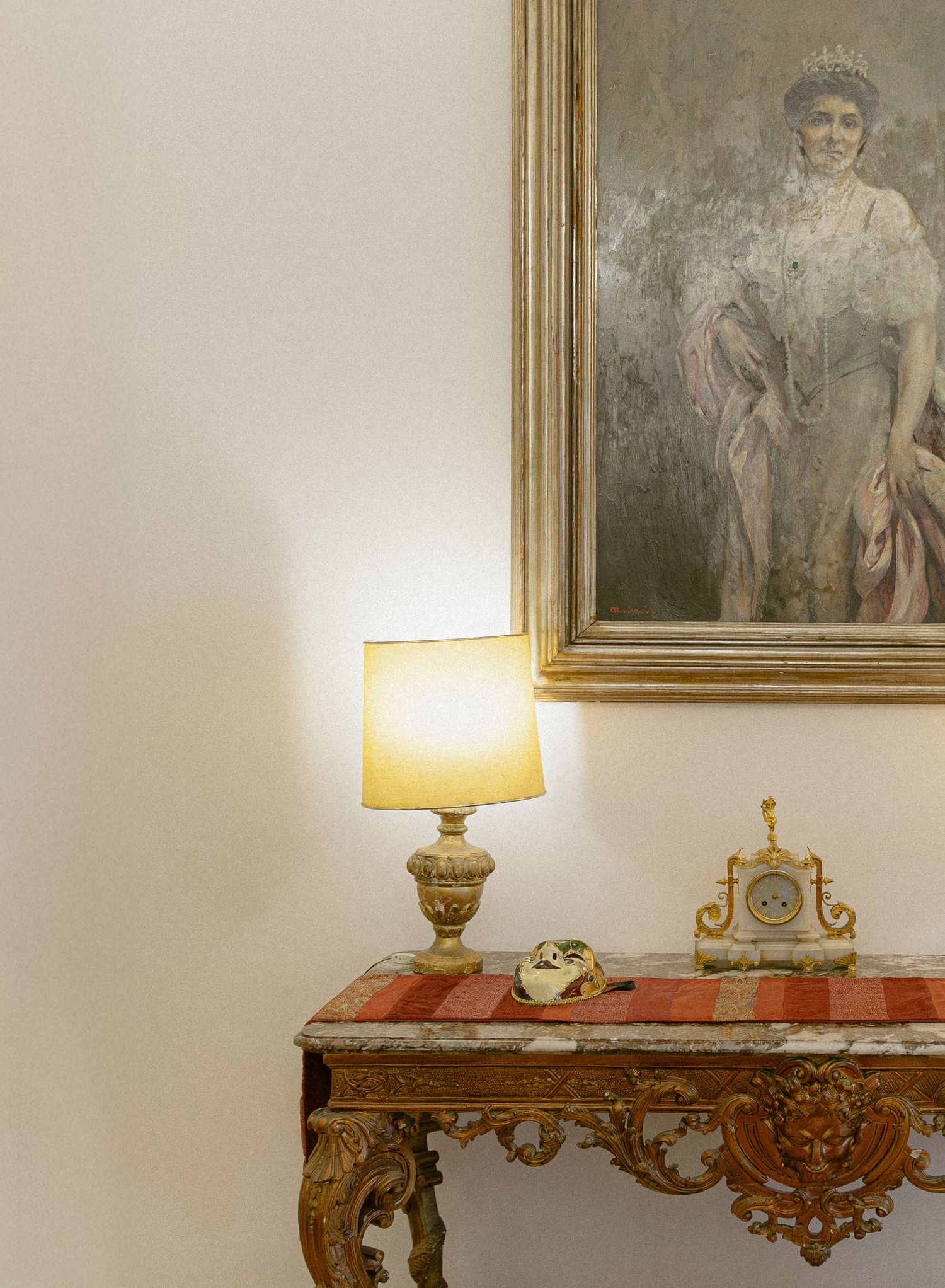 Elegant console table with gilded ornate details and table lamp displayed against a beige wall with framed artwork.