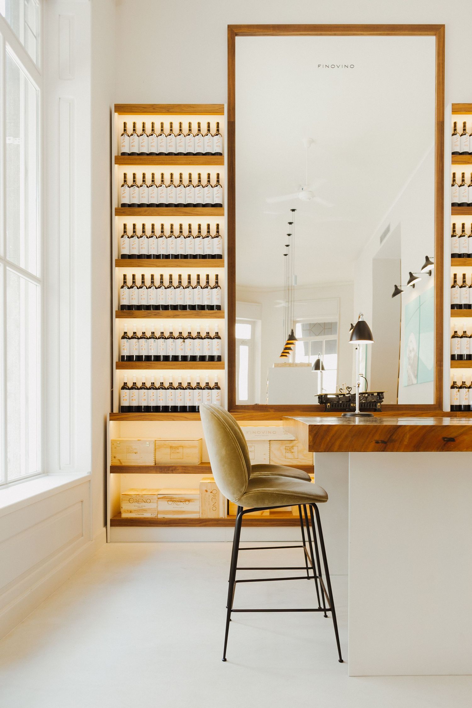 Minimalist perfume display with wooden shelves mounted on white walls and a modern accent chair in foreground.