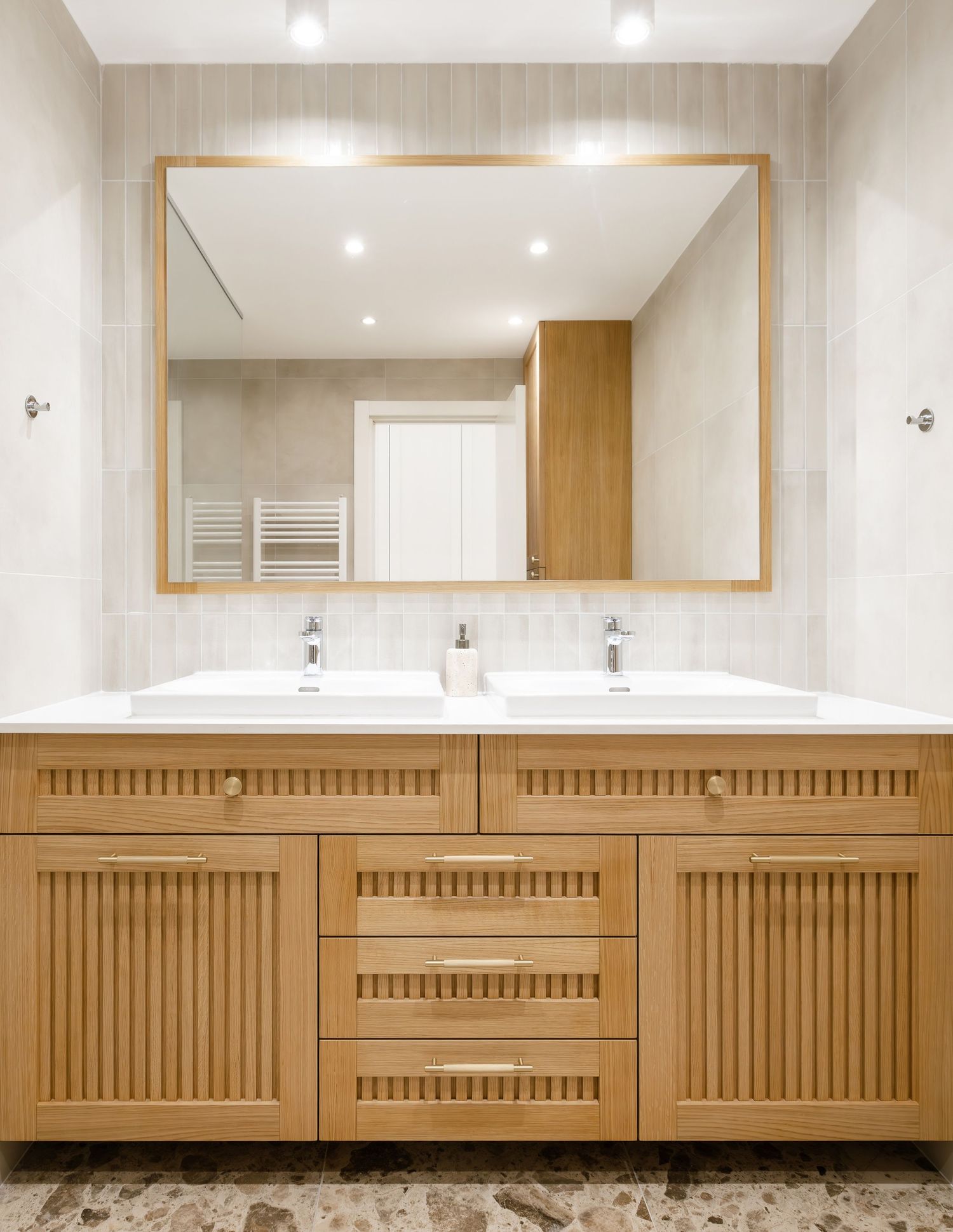 Modern bathroom vanity with wooden slatted cabinets, double sinks, and large framed mirror mounted on beige walls by Milica Prlainovic.