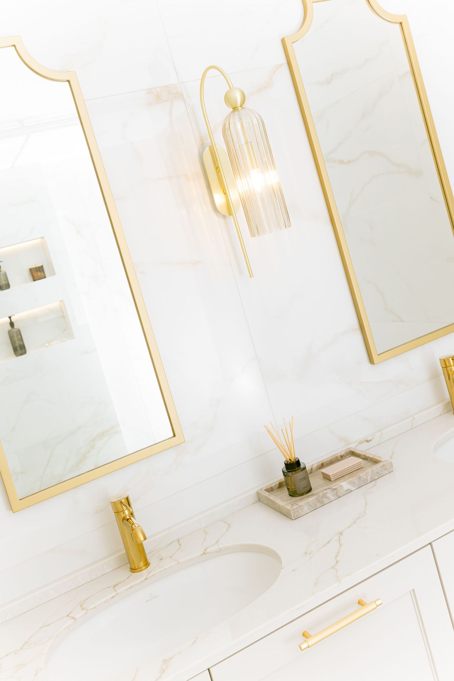 Modern white marble bathroom interior with gold accents, framed mirrors and luxurious fixtures by Vedrana Markovic.