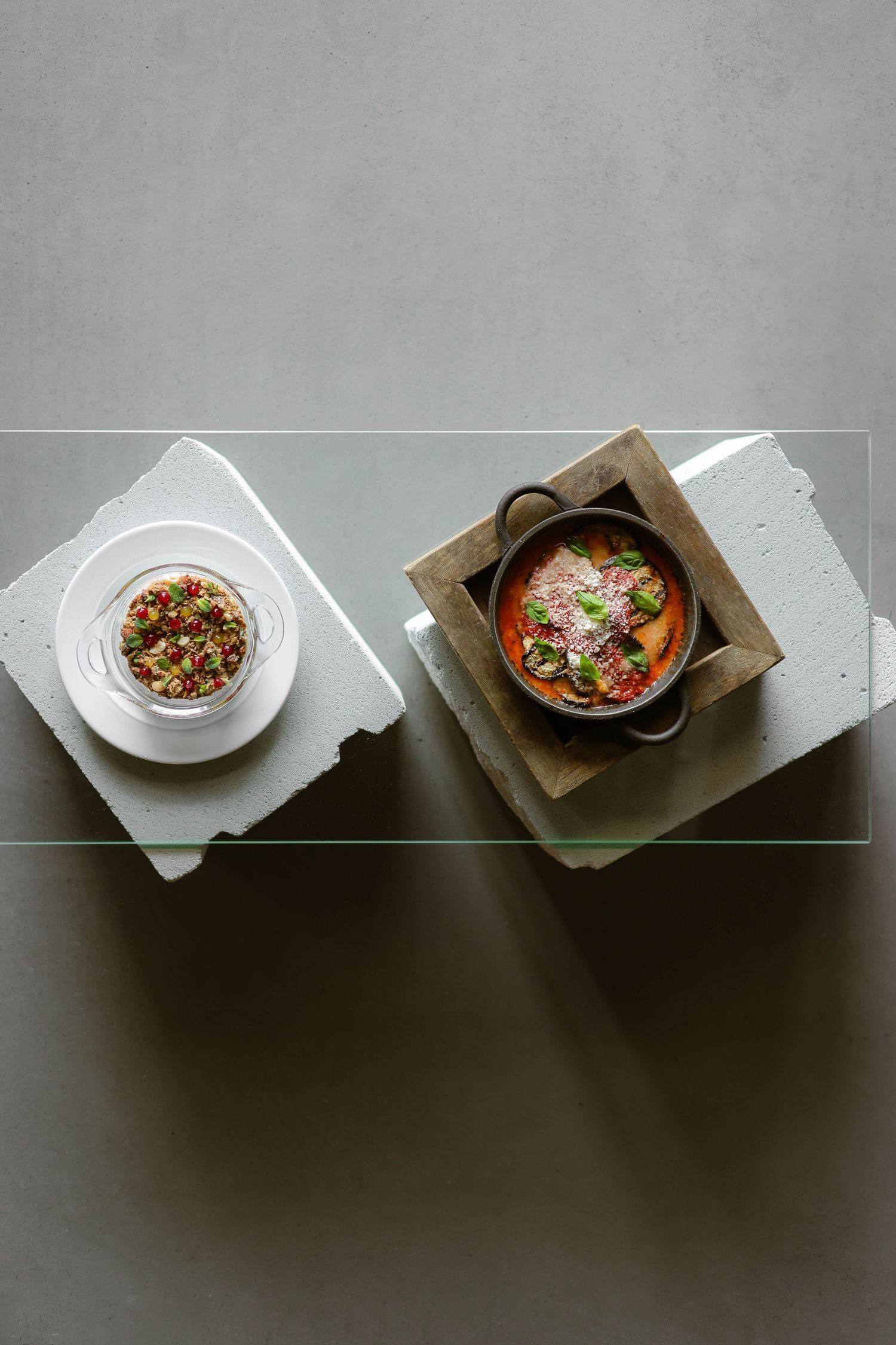 A minimalist overhead view of four plated dishes arranged diagonally on a dark surface with dramatic lighting.