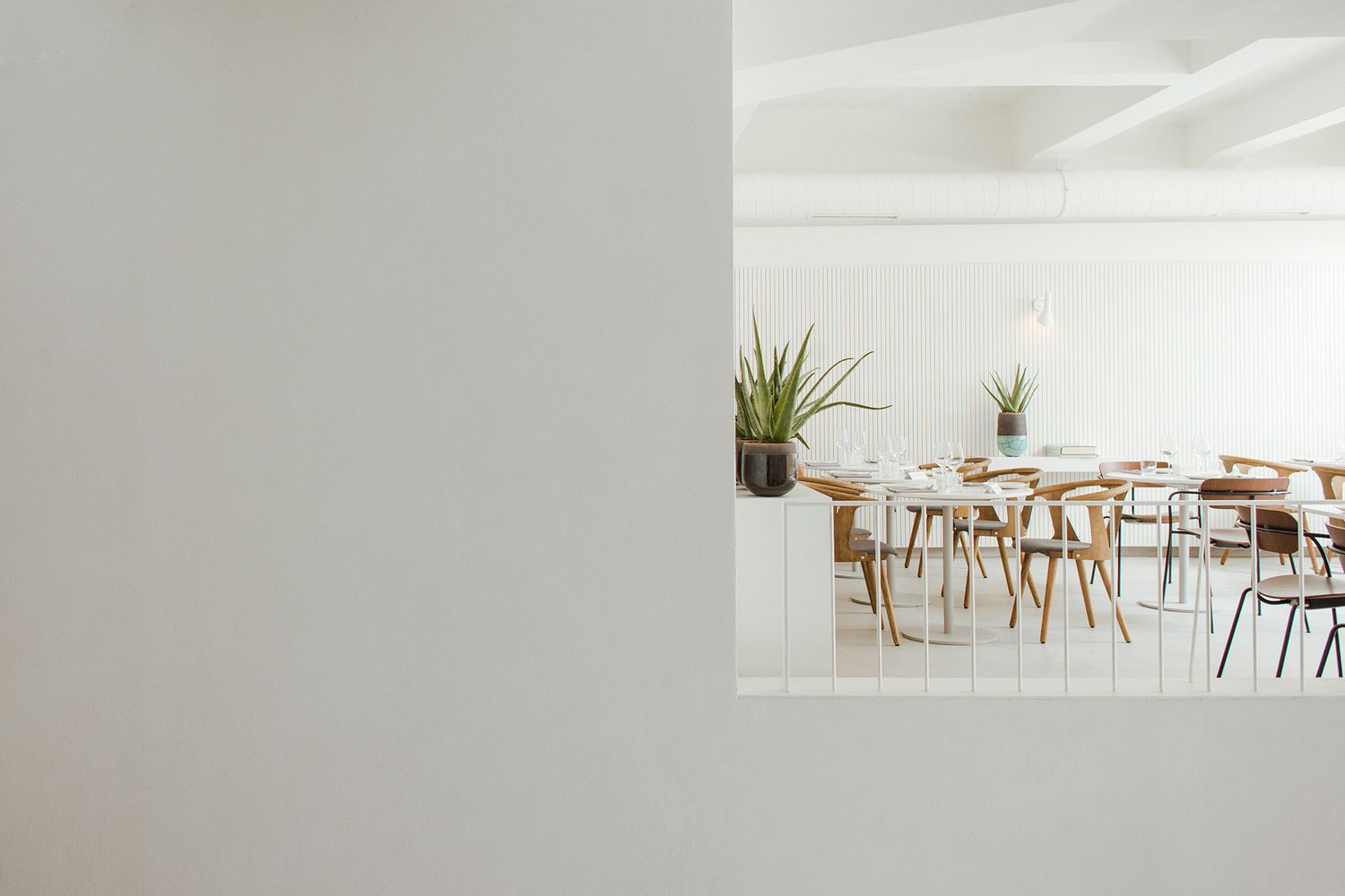 Minimalist white restaurant with wooden chairs and tables arranged in a clean, modern restaurant setting in Beton Hala, Belgrade, Serbia.
