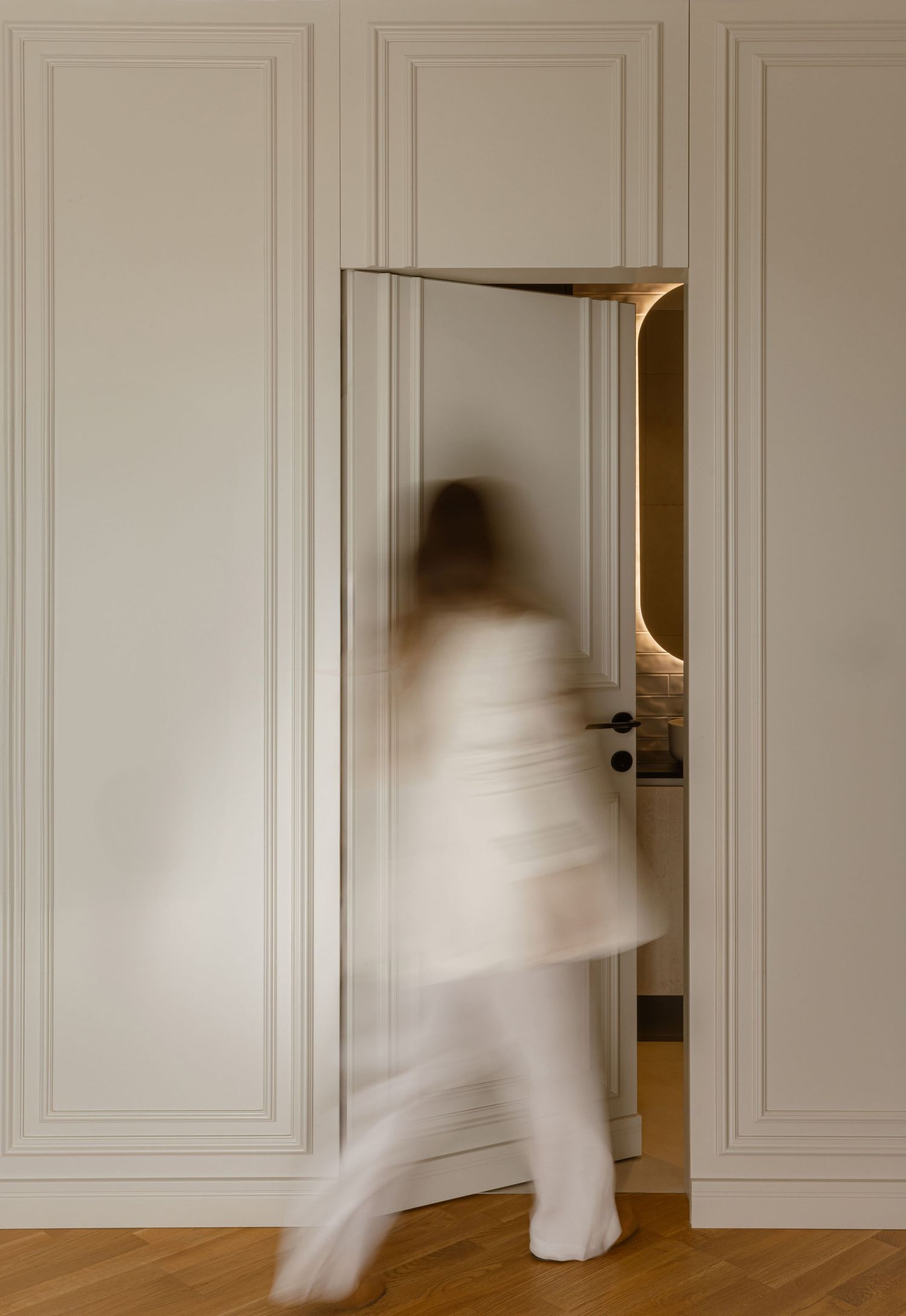 Long exposure photo shows blurred motion of person in white walking through modern interior with white paneled walls by Vedrana Markovic.