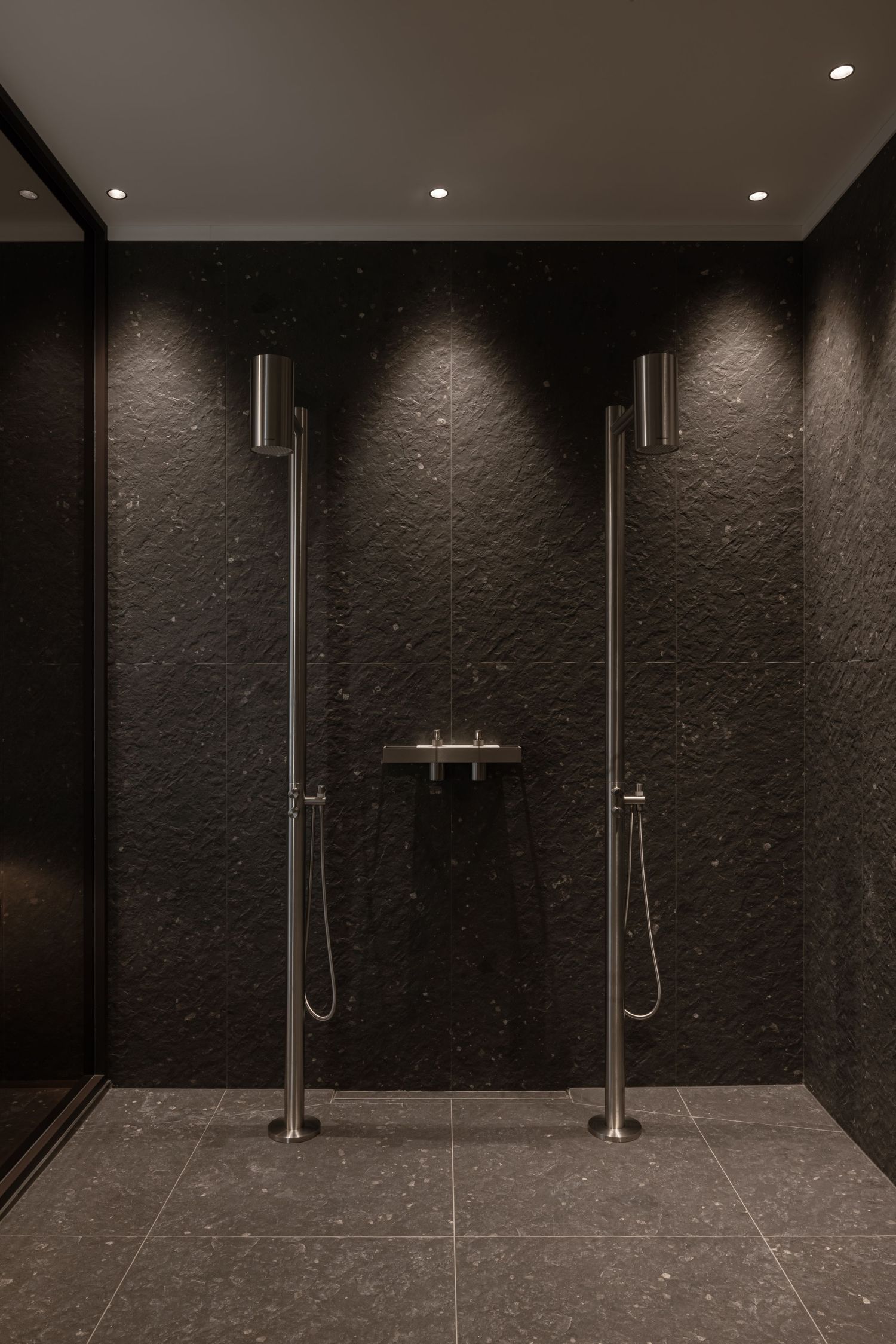 Modern minimalist shower room with dark textured walls and dual rainfall showerheads in sleek stainless steel finish by Aleksandar Savikin.