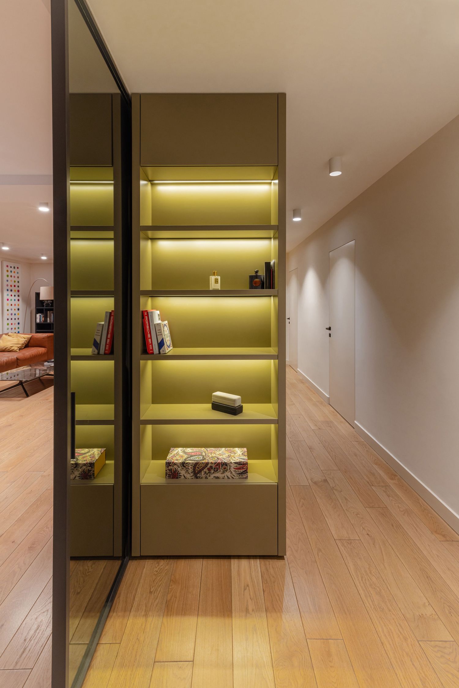 Modern minimalist hallway with wooden flooring and illuminated green wall niche displaying decorative items by Studio Fluid.