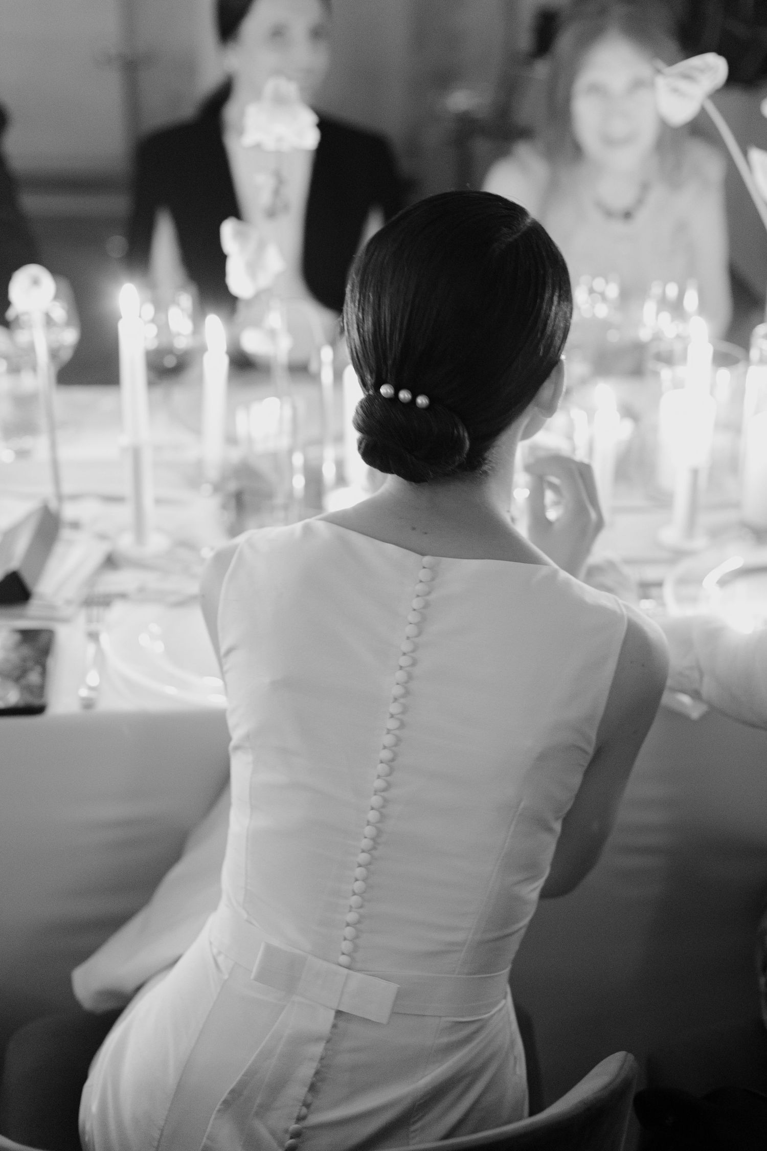 A series of black and white photos showing the back of a bride's dress with delicate button details at a wedding reception.