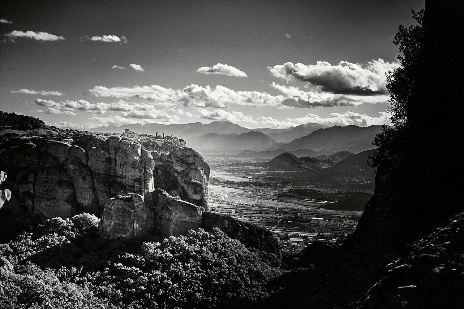 Dramatic black and white panoramic view of mountain peaks and valleys under scattered clouds at sunset.