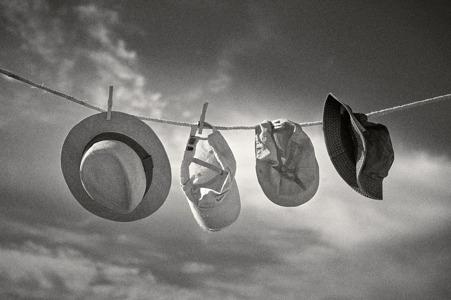 Hats hanging on clothesline against dramatic cloudy sky in black and white artistic photography.