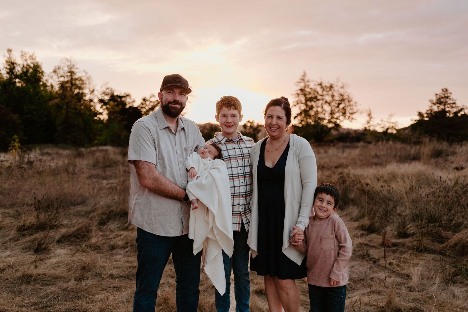 Family of four posing together outdoors during sunset in natural setting.