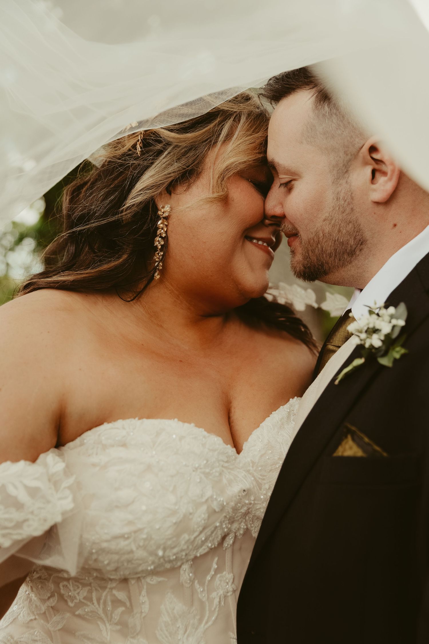 Intimate wedding portrait of newlyweds in a close romantic embrace, with bride in lace gown and groom in black suit.