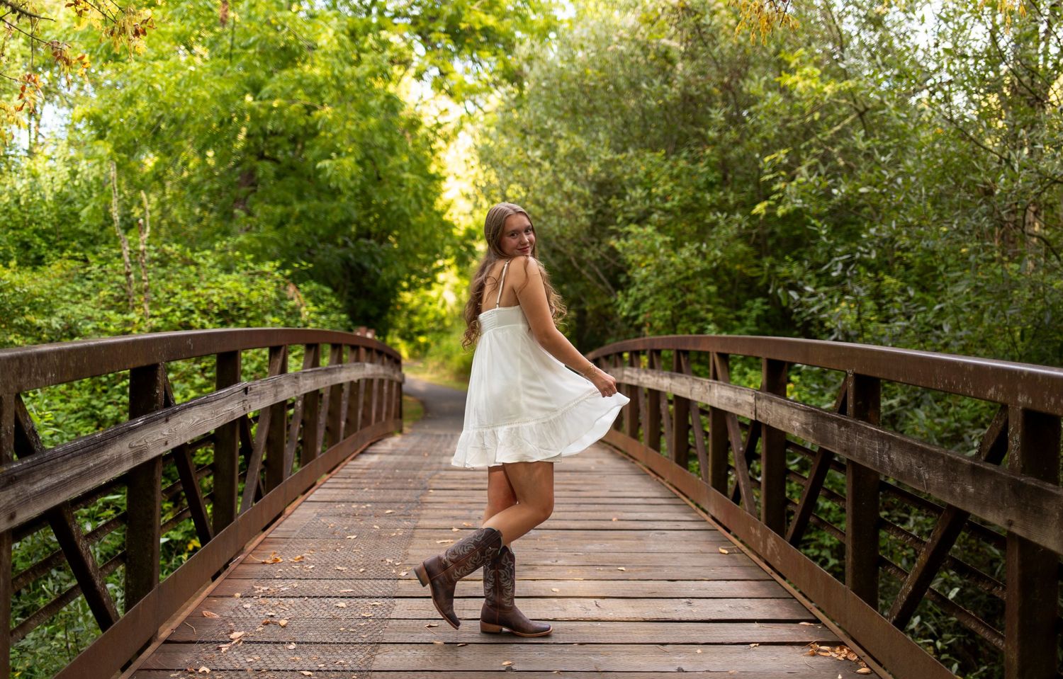 Person in white dress twirling on wooden bridge surrounded by lush greenery.