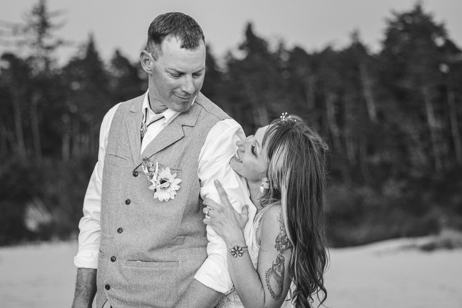 A romantic black and white photo of a couple sharing a light-hearted moment together outdoors near a forest.