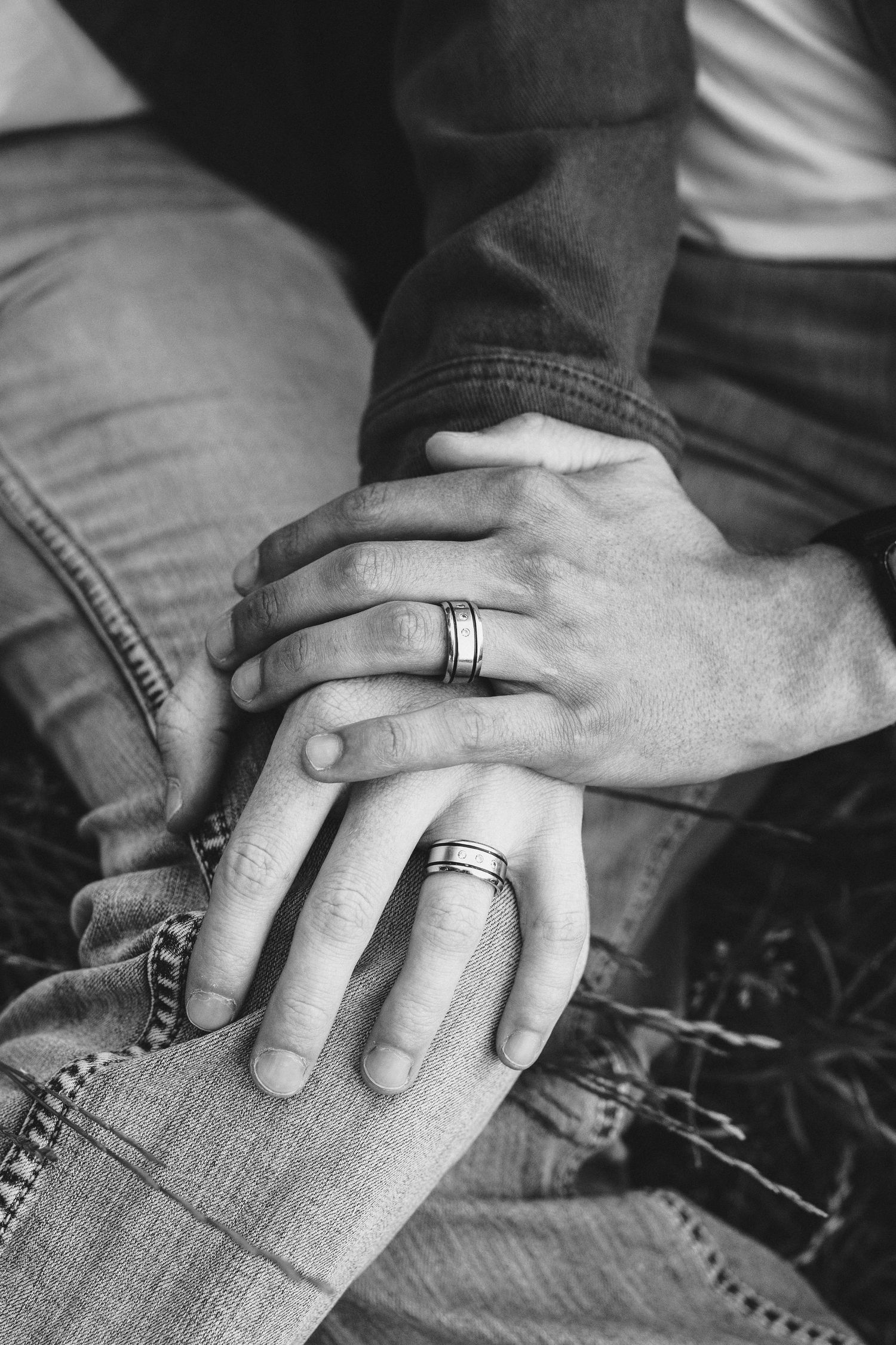 Black and white close-up of hands with wedding rings intertwined on denim jeans, symbolizing love and commitment.