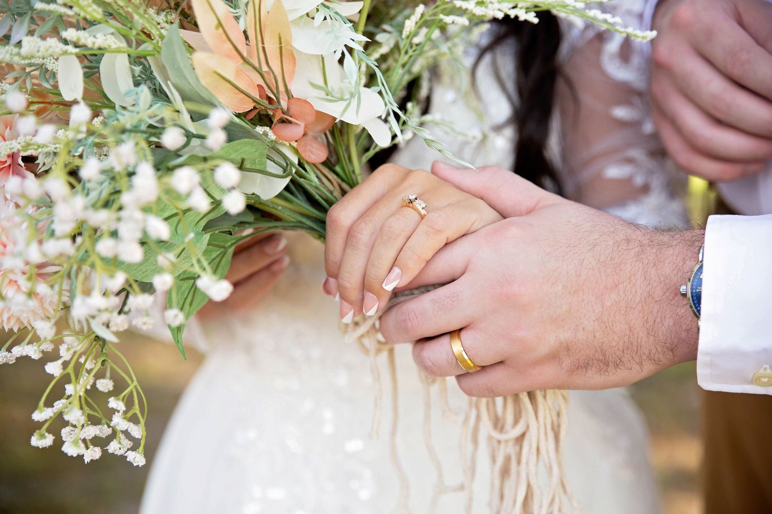 Close-up view of hands holding delicate white and peach floral bouquets with greenery accents.