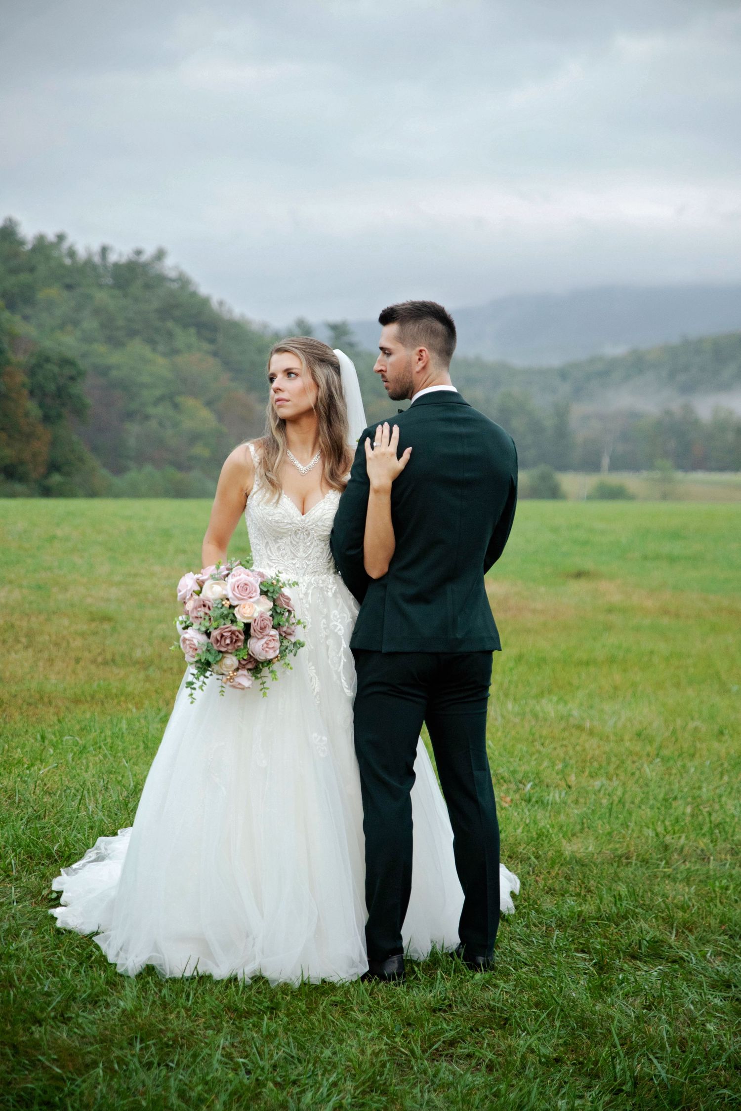 A couple in wedding attire stands in a misty green field during their romantic outdoor photo session.
