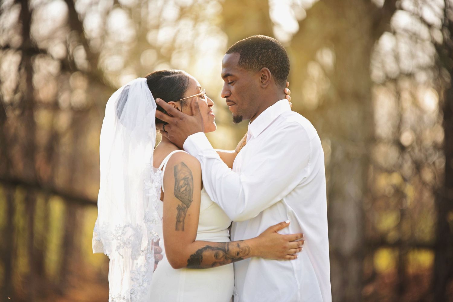 A bride and groom share an intimate moment in a sunlit forest setting during their wedding ceremony.