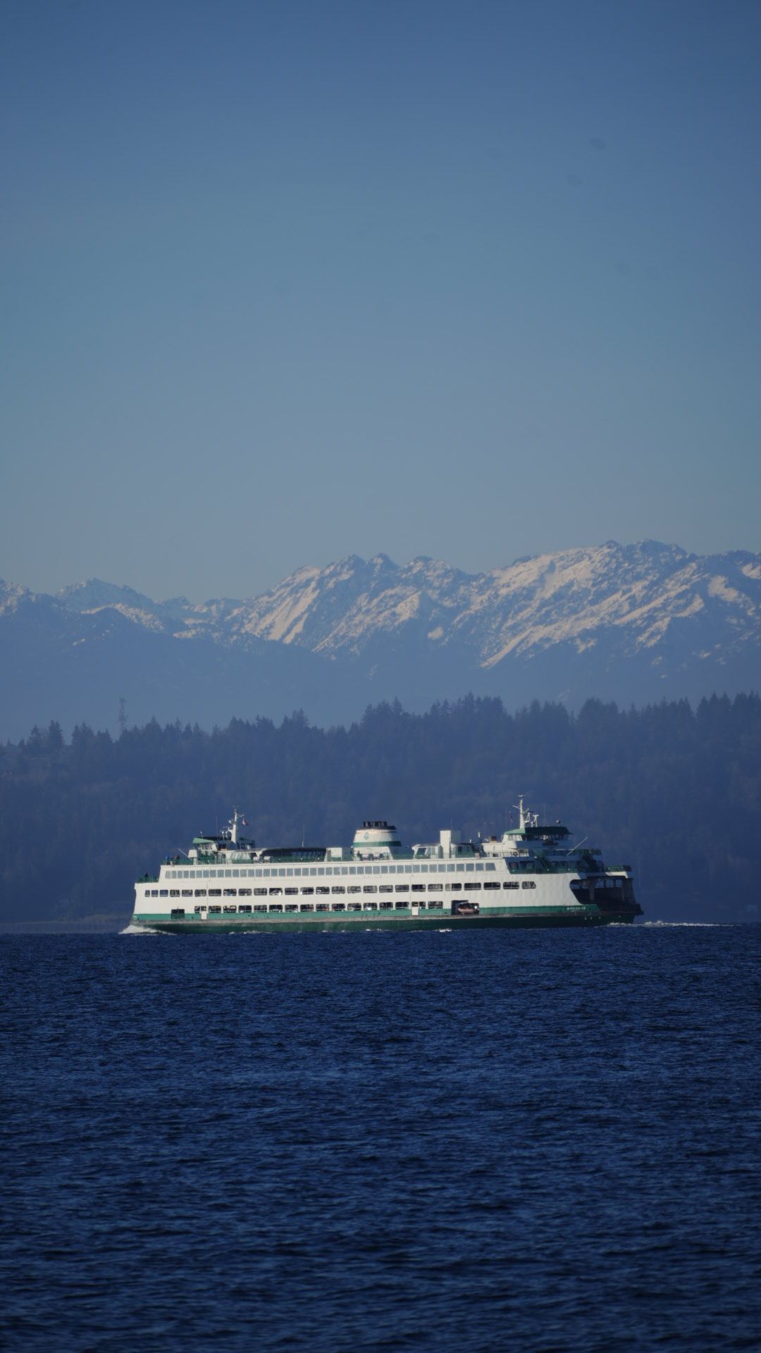 Washington State ferry crosses Puget Sound with snow-capped Olympic Mountains in background on clear day.