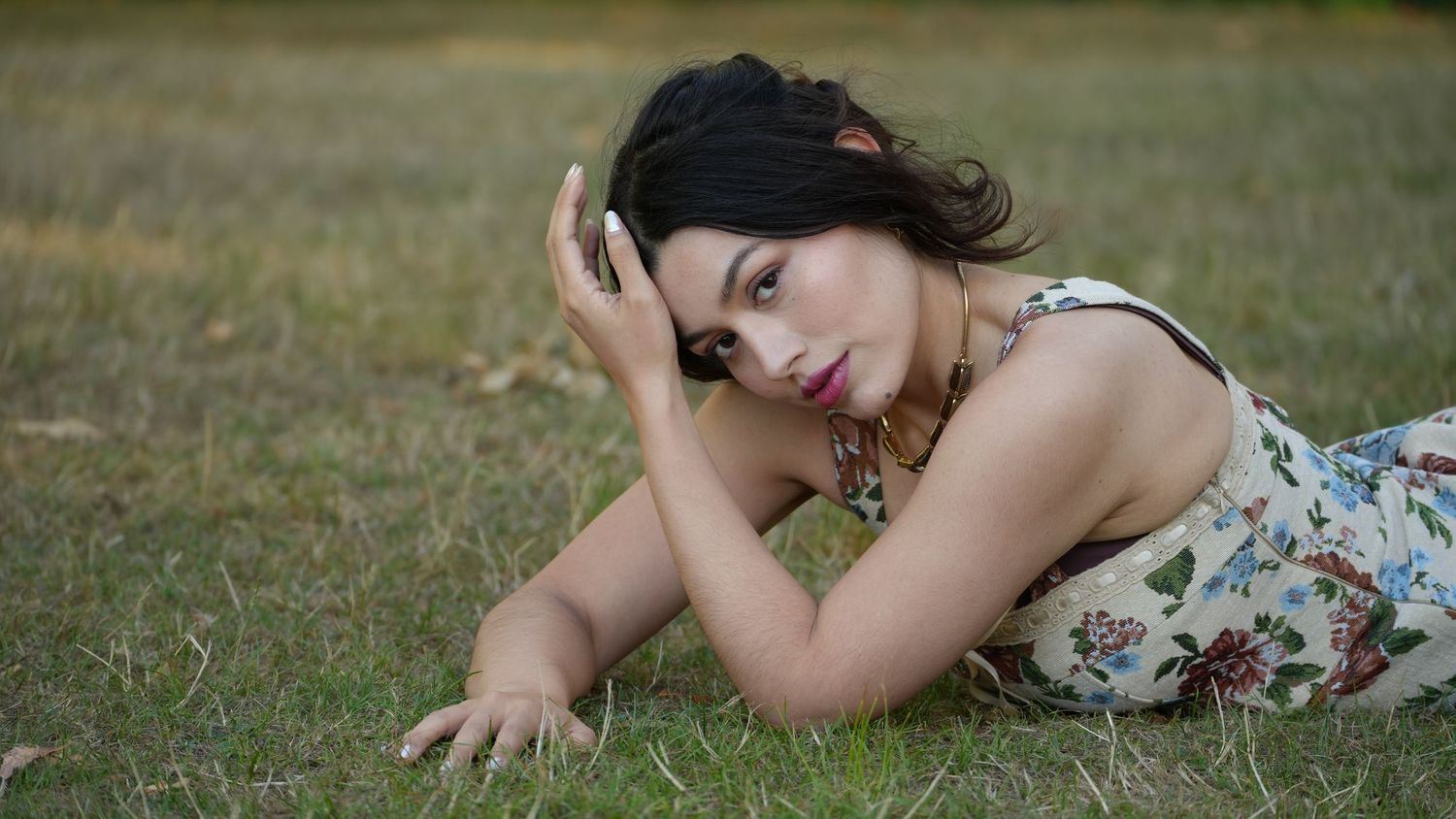 Person lying on grass in playful poses wearing summer dress, with floral pattern and ring details.