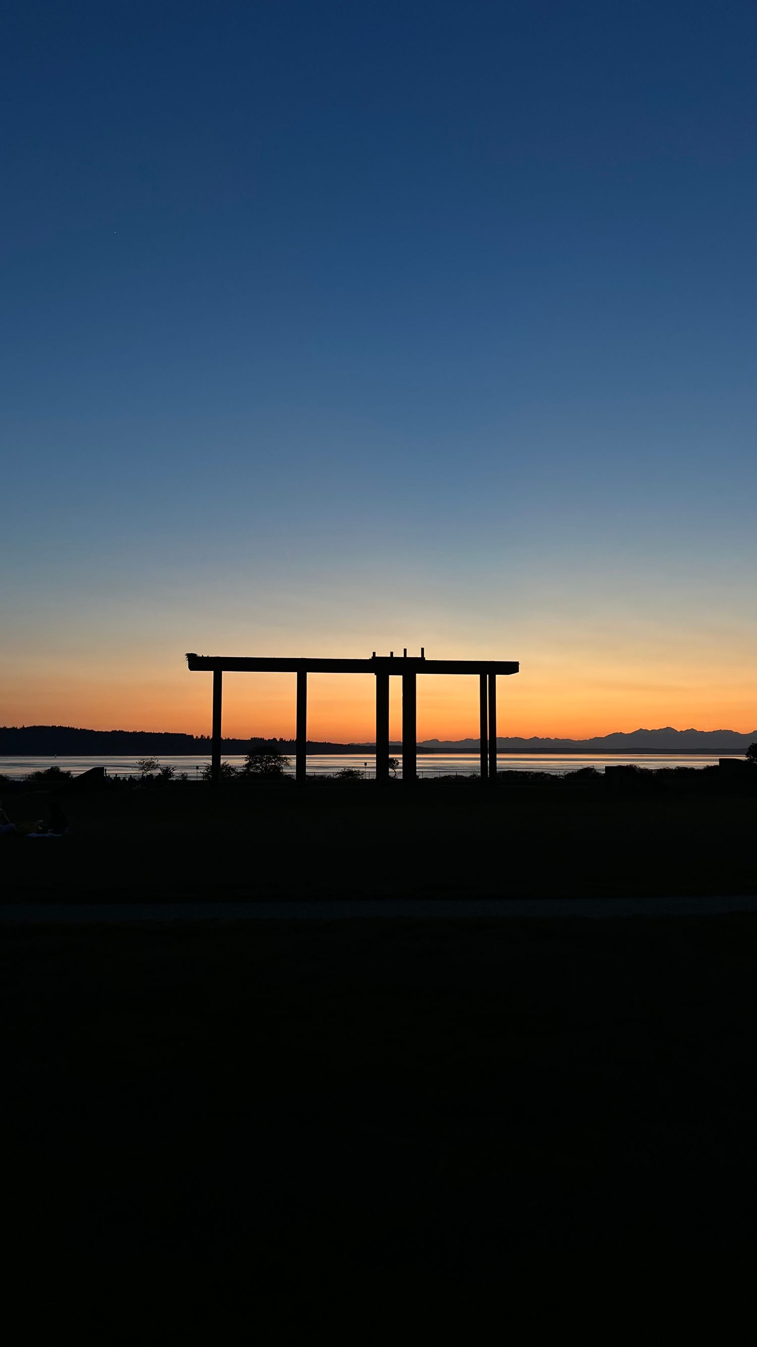 Silhouette of wooden posts against vibrant orange and blue sunset sky with mountain range in the distance.