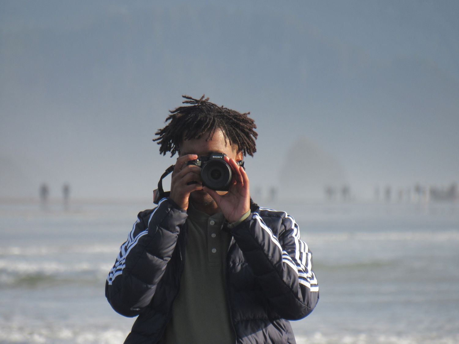 A person looks through binoculars while standing on a beach during an overcast day.