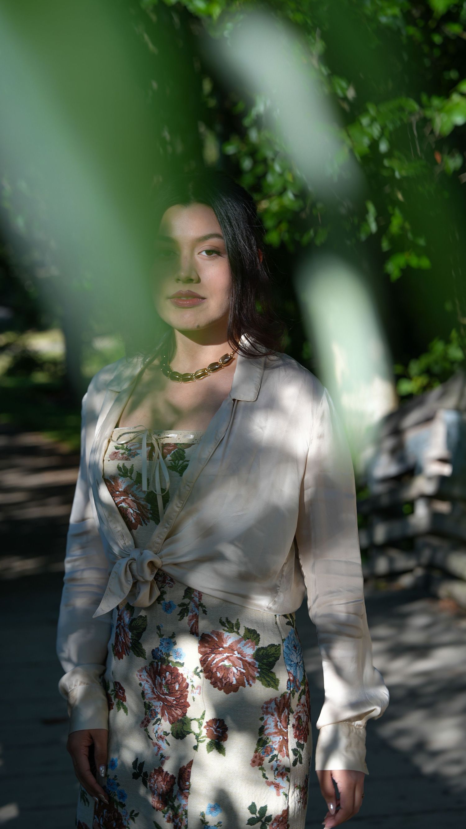 Sun dappled portrait session in white floral dress surrounded by lush green foliage and garden shadows.