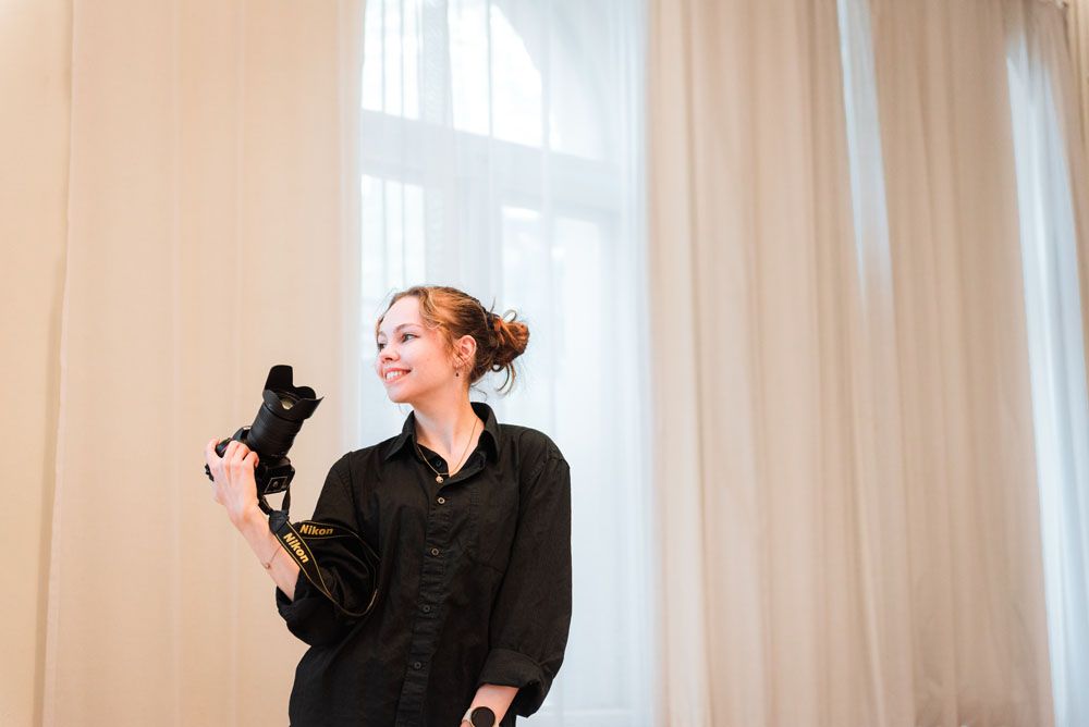 Valokuvaaja Anniina Virtanen kamera kädessä ja hymyilemässä valokuvausstudiollaan Turun keskustassa.