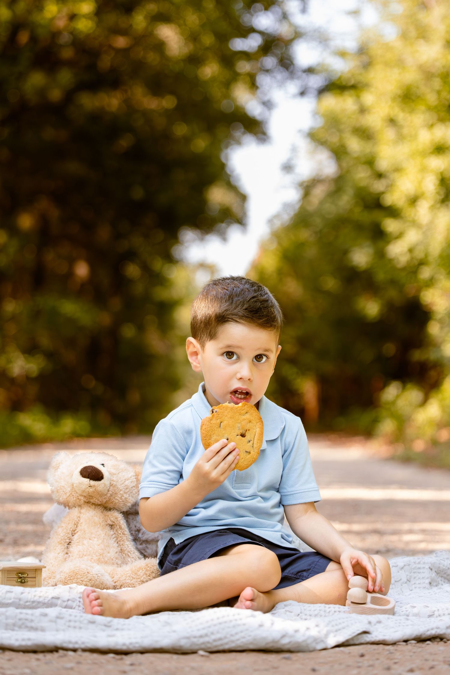 Child enjoying snack time with teddy bear companion on picnic blanket outdoors. Fort Worth milestone photoshoot, Southlake photographer
